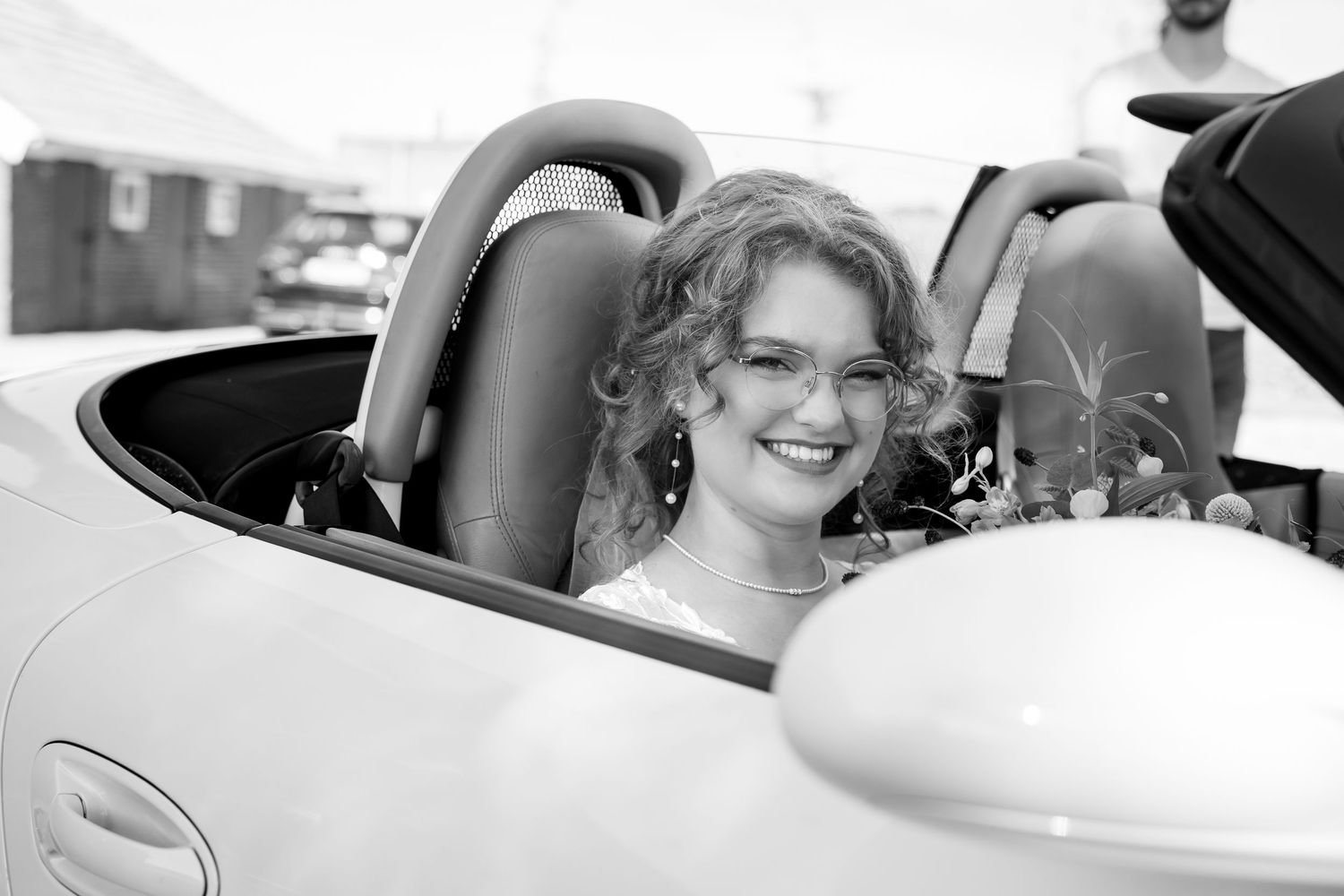 A classic black and white photo of someone smiling in a convertible car.