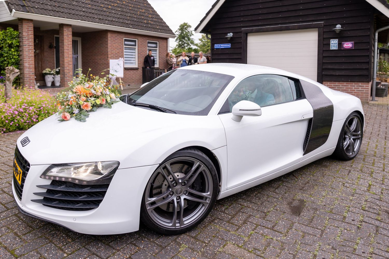A white Audi R8 sports car parked in a driveway with brick house in background.