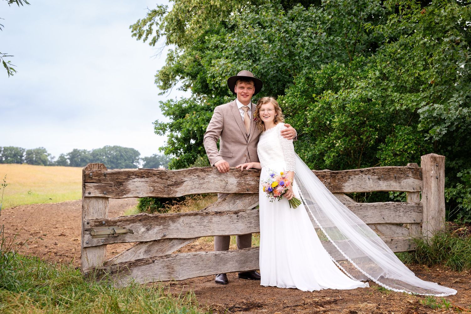 A countryside wedding portrait featuring a rustic wooden gate and flowing white veil.