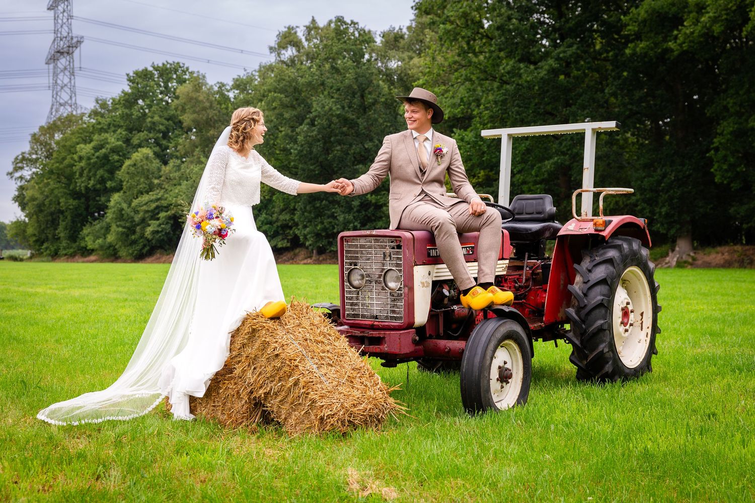 A countryside wedding scene with a vintage tractor and hay bale in a lush green field.