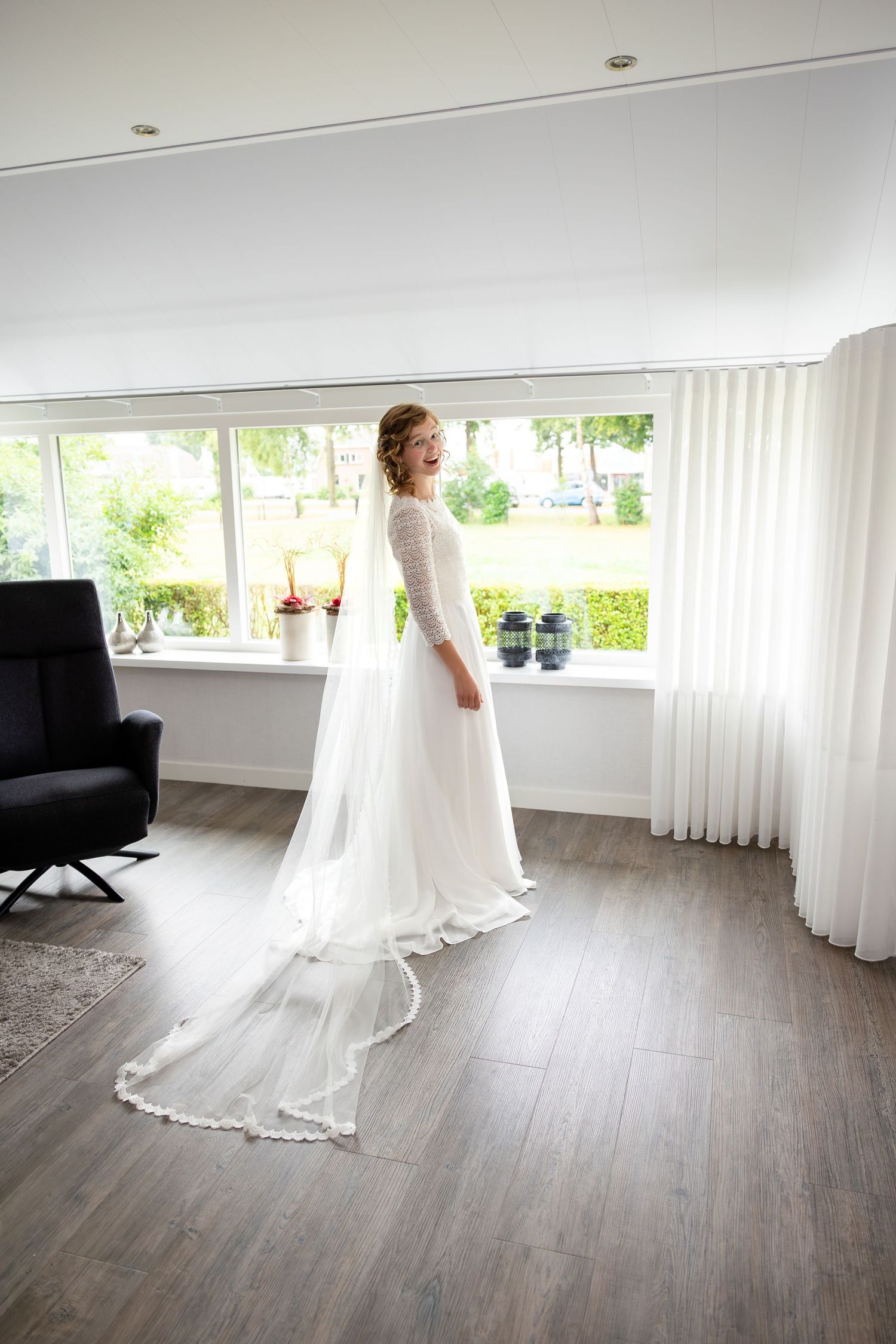 A flowing white wedding dress moves gracefully across a modern room with wooden floors.