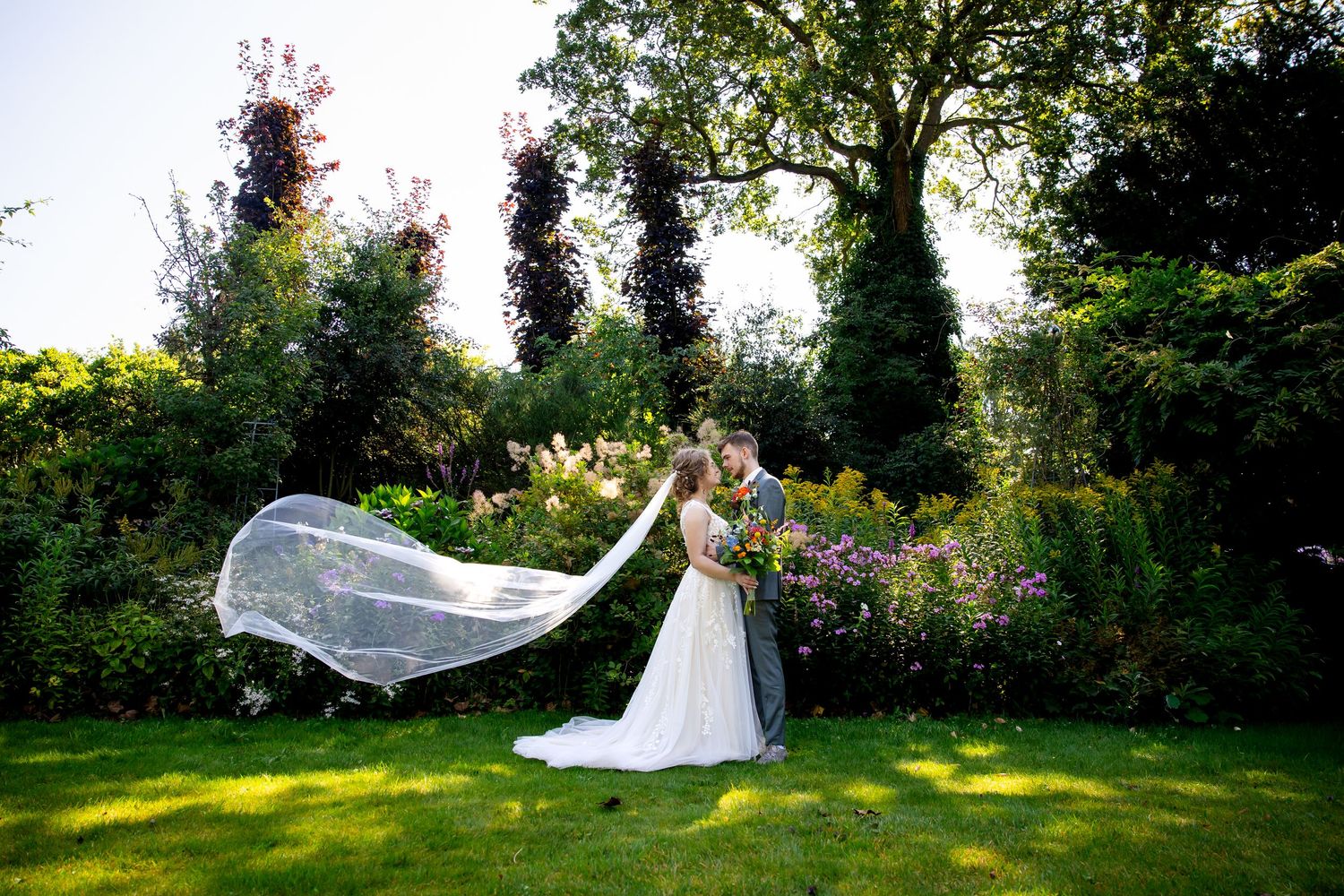 A flowing veil catches the wind in this romantic garden wedding photo.