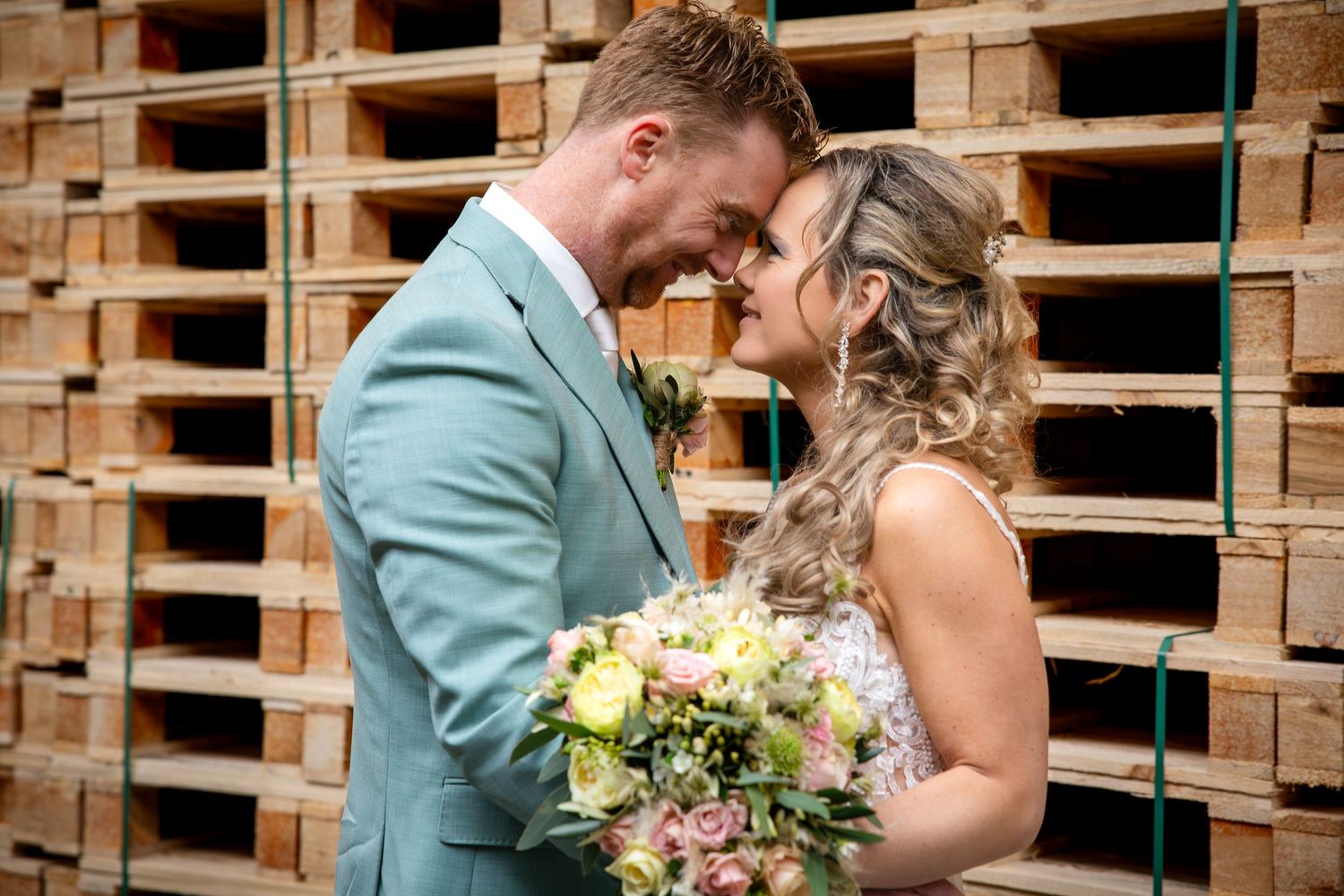 A couple shares a romantic kiss in front of a rustic wooden pallet wall at their wedding ceremony.