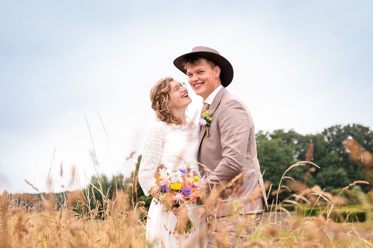 A romantic countryside wedding portrait with colorful bouquet against golden wheat field.