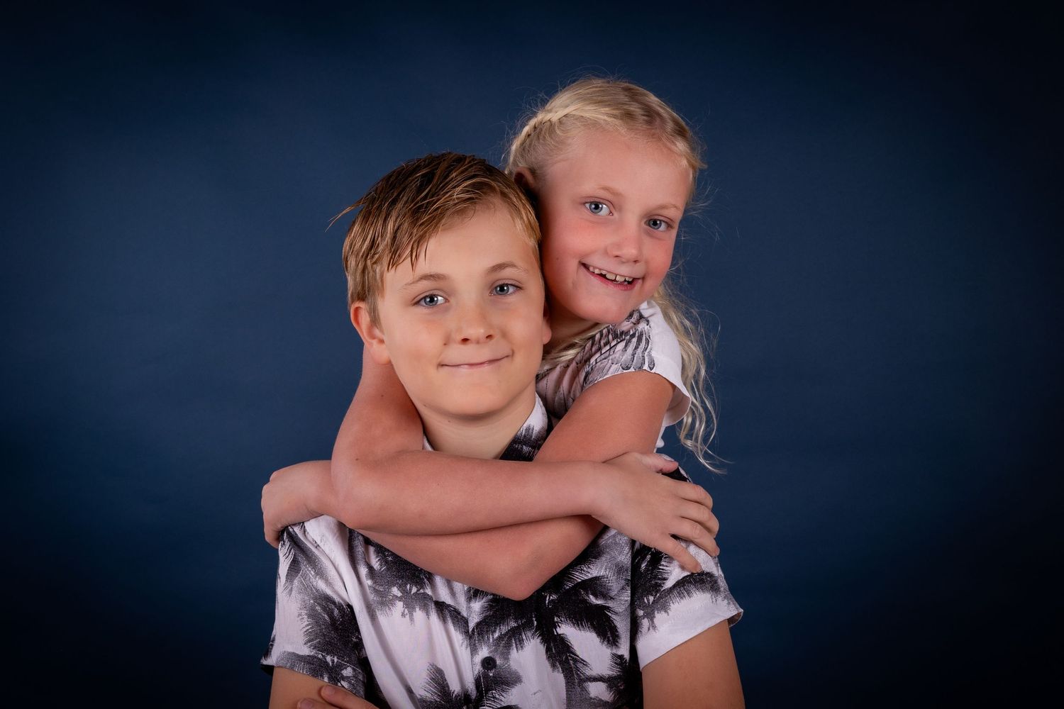 Siblings embracing and smiling for a portrait against navy studio backdrop.