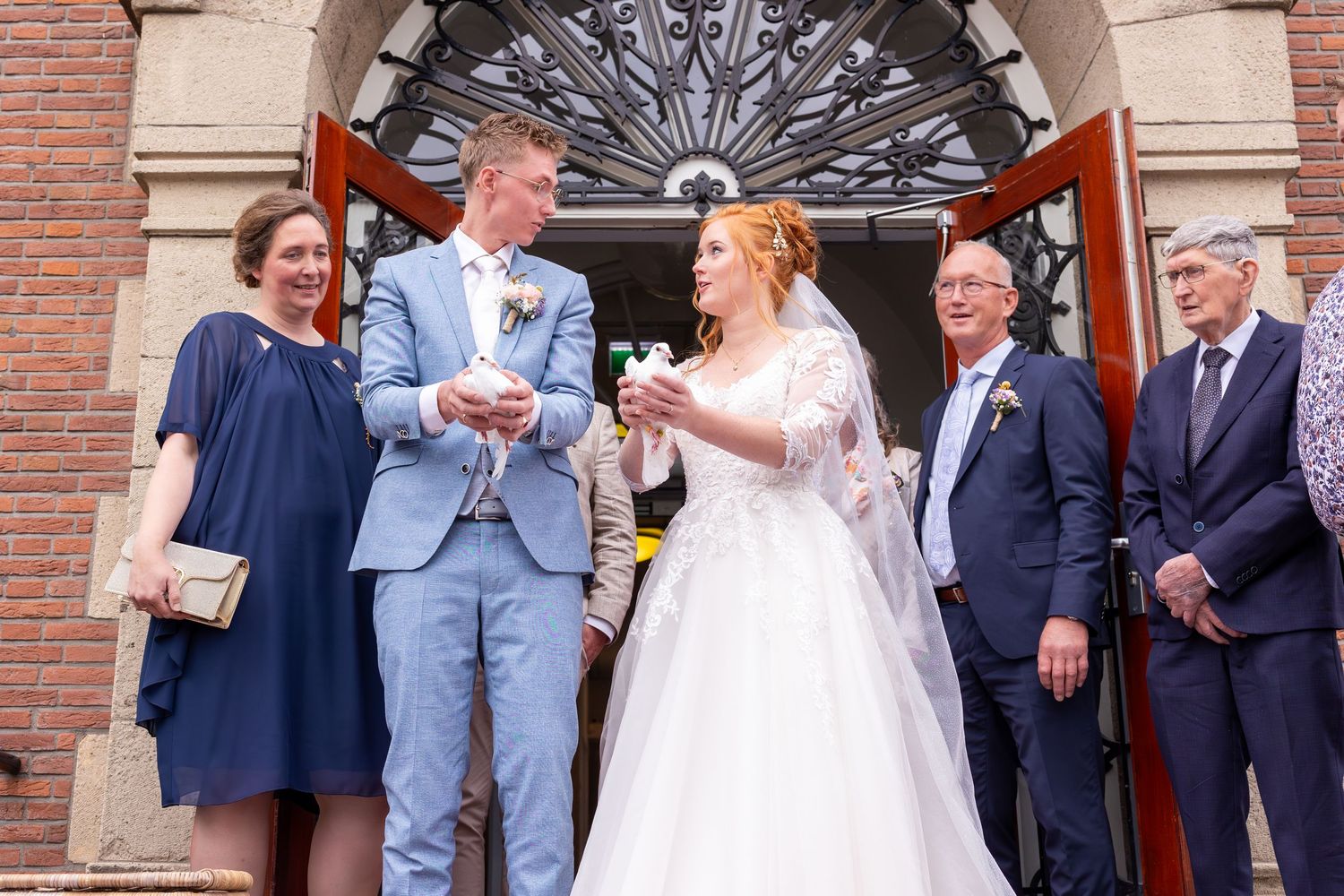 pasgetrouwd stel laat twee witte duiven los en gasten kijken toe voor het gemeentehuis met rode loper