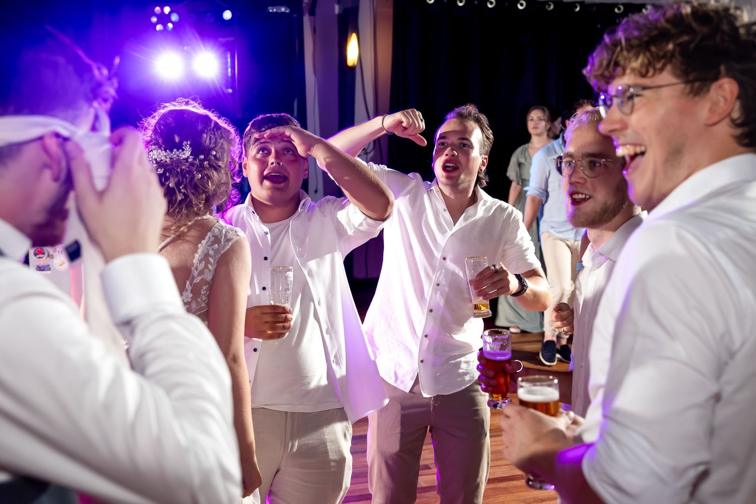 Wedding celebration with guests dancing under vibrant purple lighting.