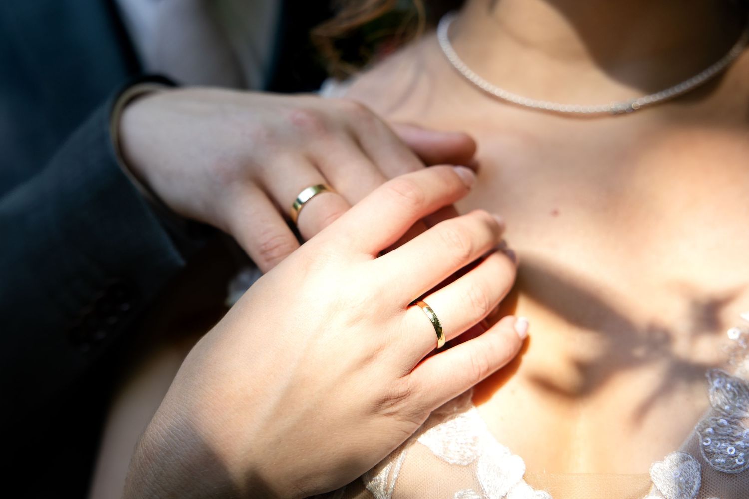 Soft sunlit close-up of hands and wedding rings against delicate fabric.
