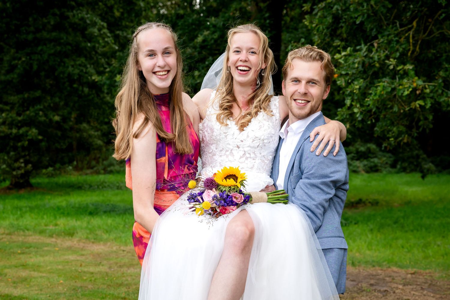 bruidspaar met broer en zus met kleurrijke kleding in een natuurlijke buitenomgeving.