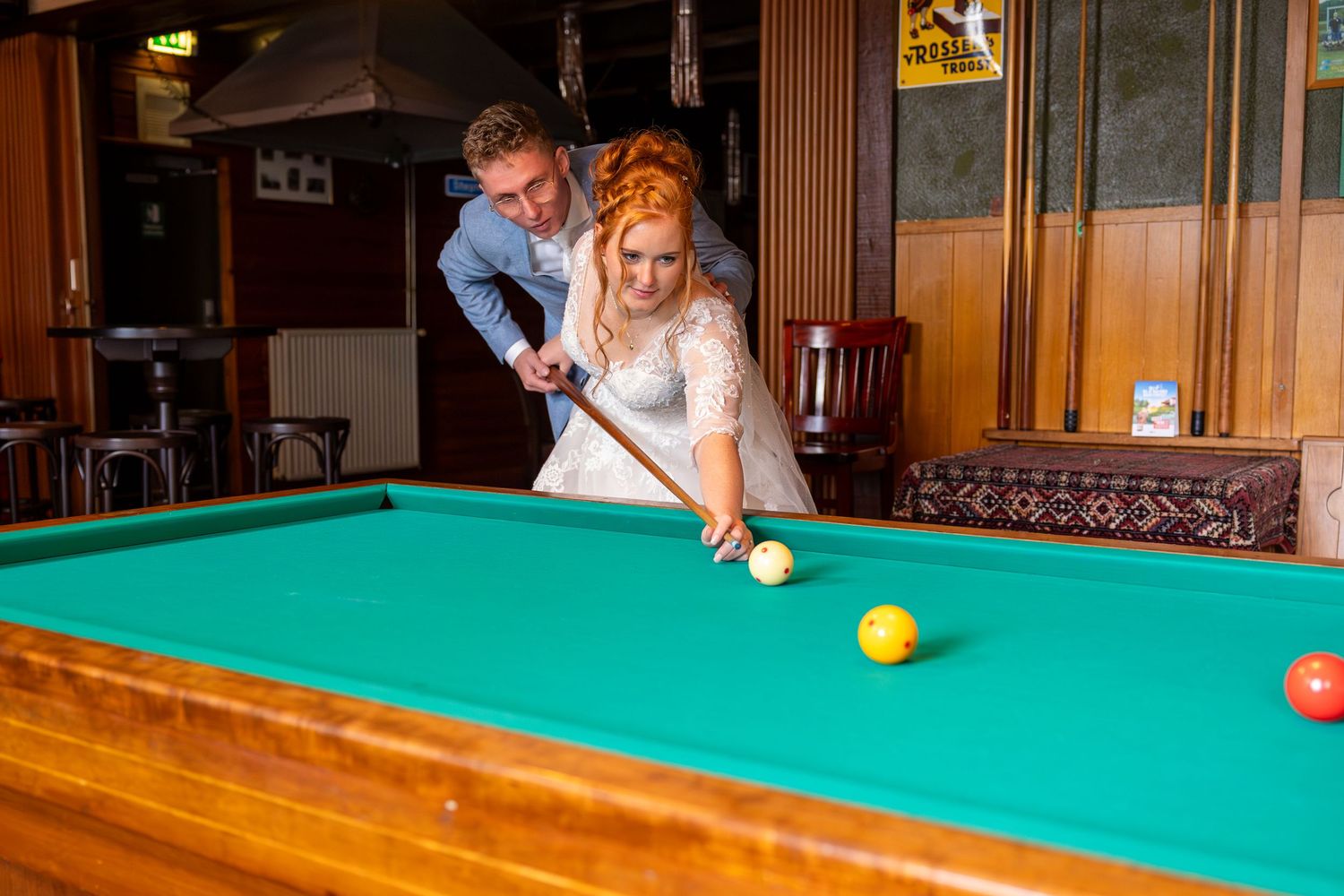 A couple plays pool together in formal attire at a pub.