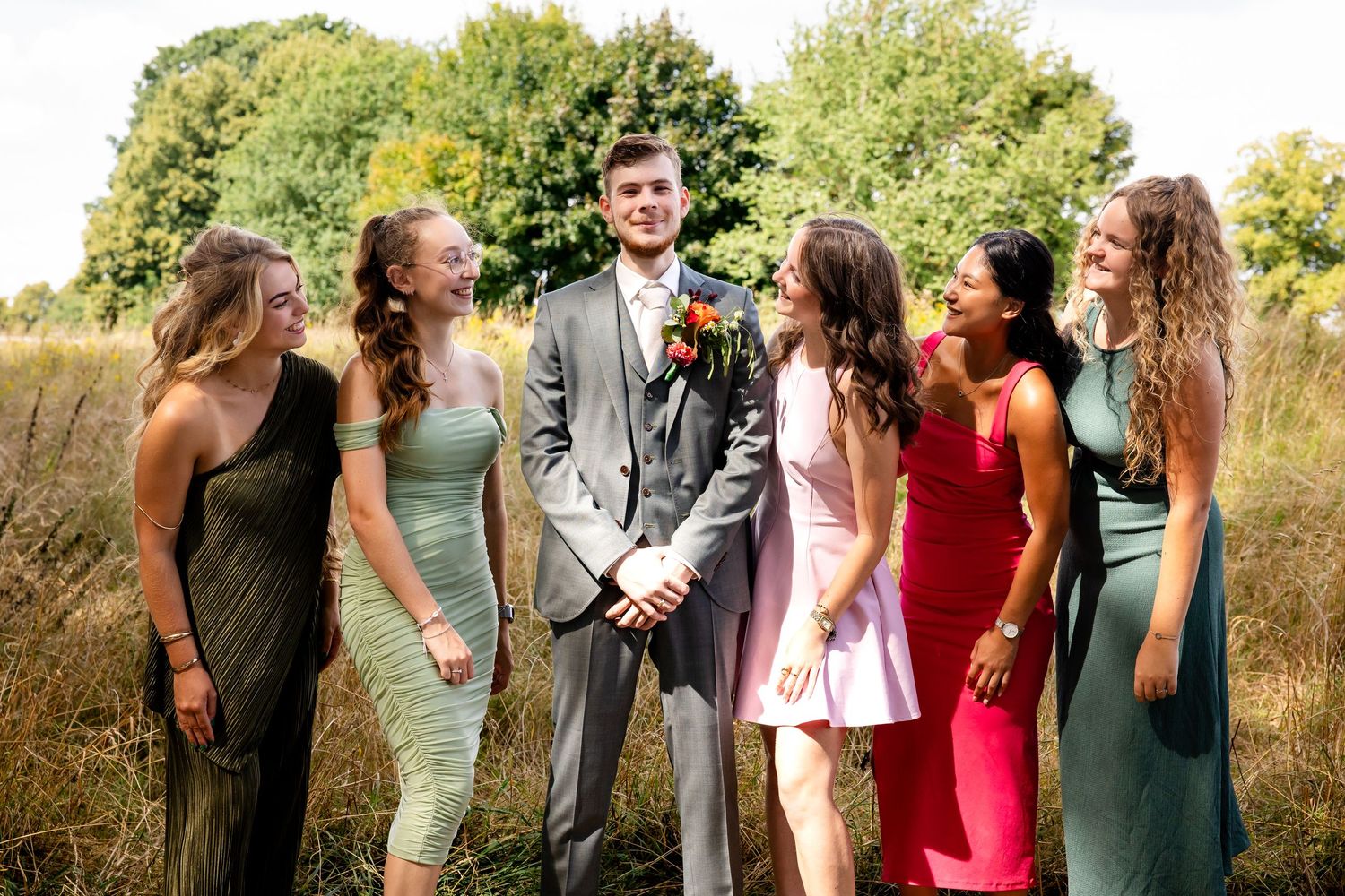 Wedding party members interact and laugh together in outdoor setting.