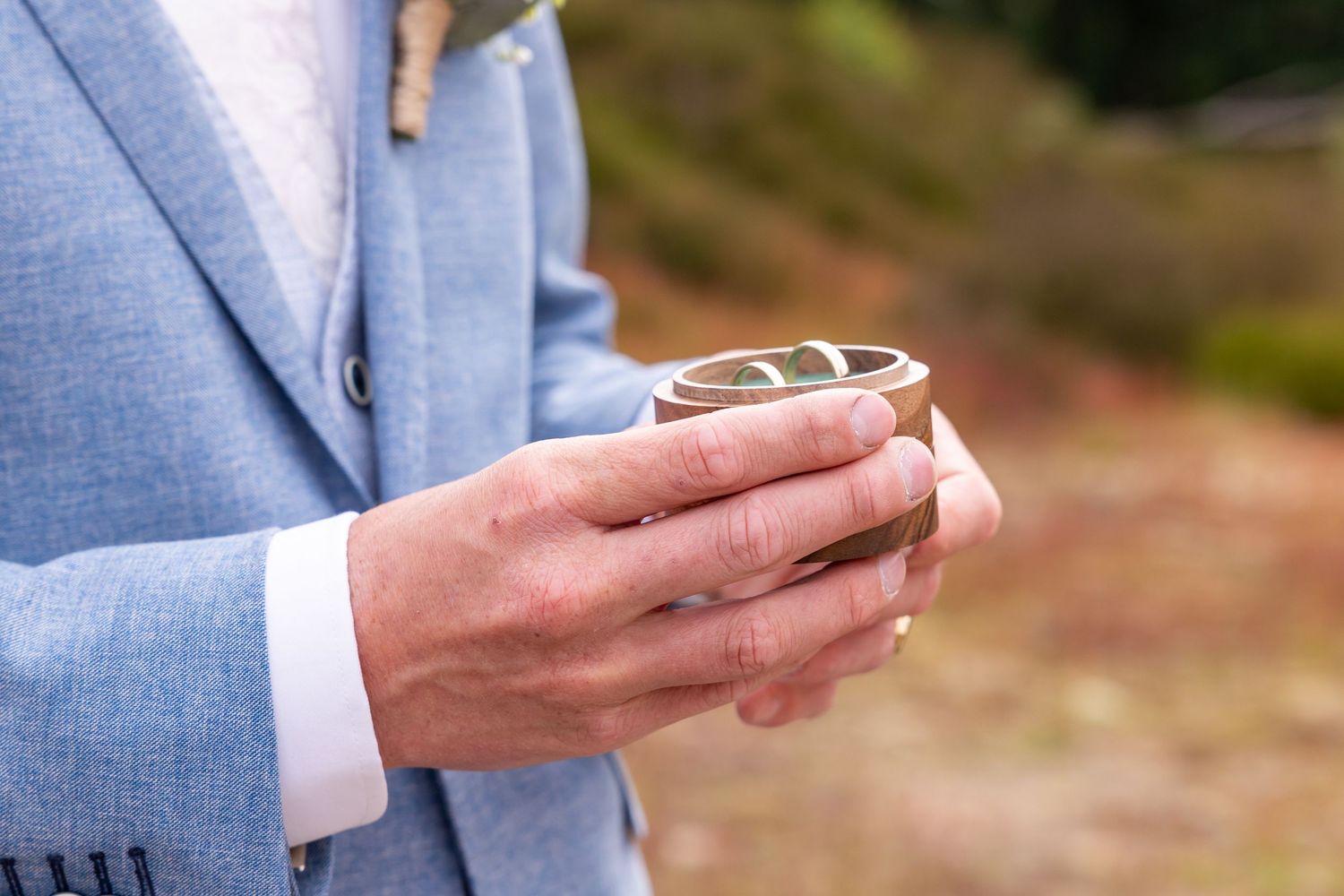 Close-up of hands holding wedding rings against a light blue suit jacket.
