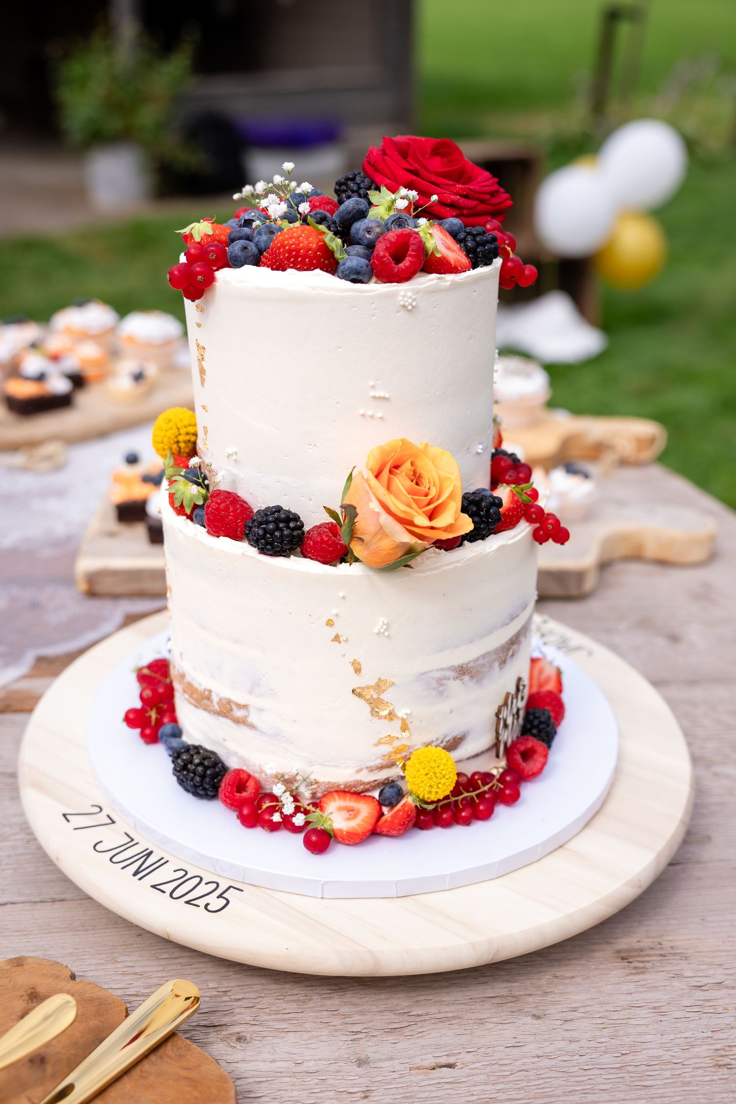 Elegant white wedding cake adorned with fresh berries, flowers, and fruit on a rustic wooden table.