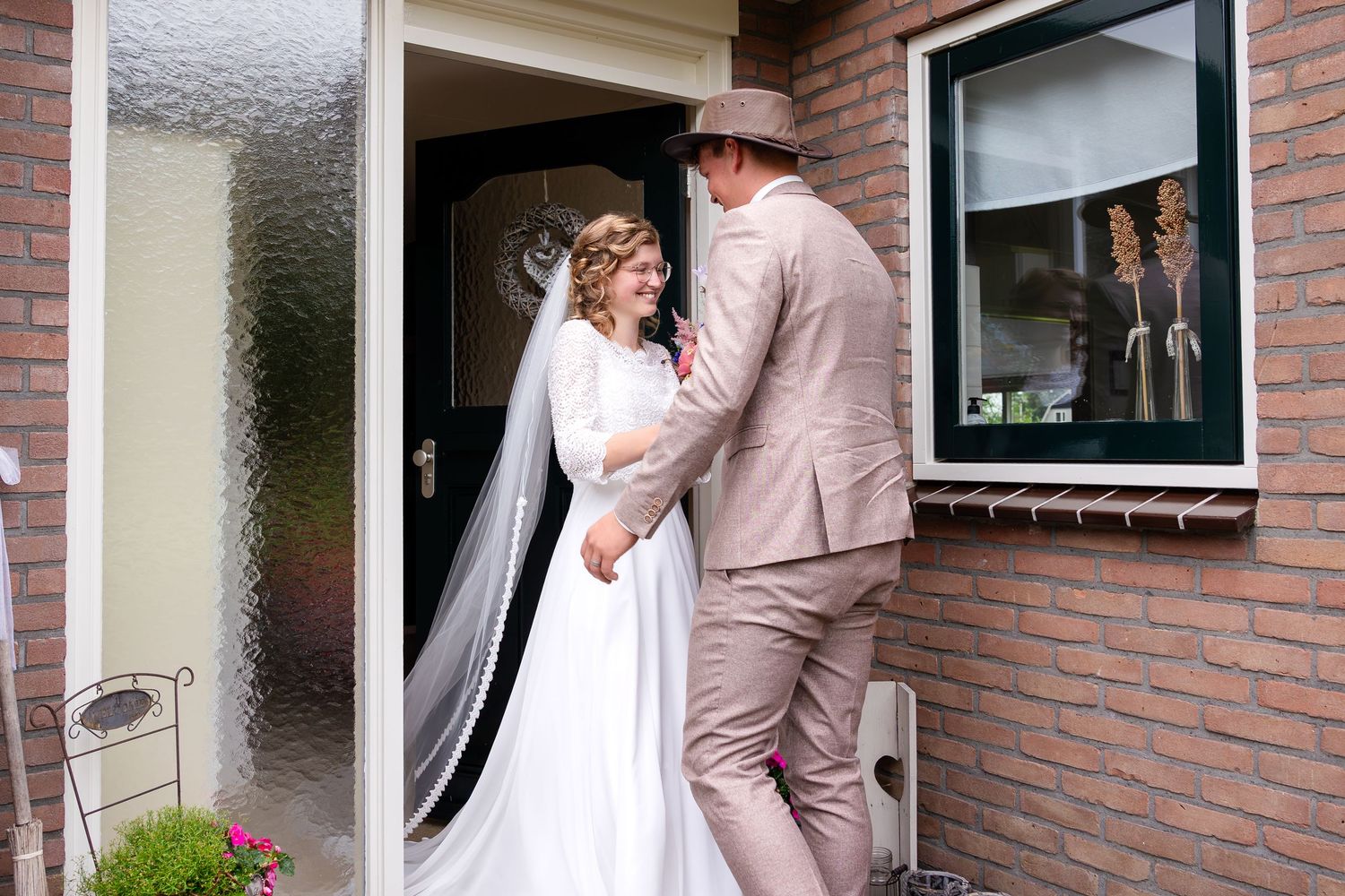 A couple shares a moment outside a brick home with a classic car in view.