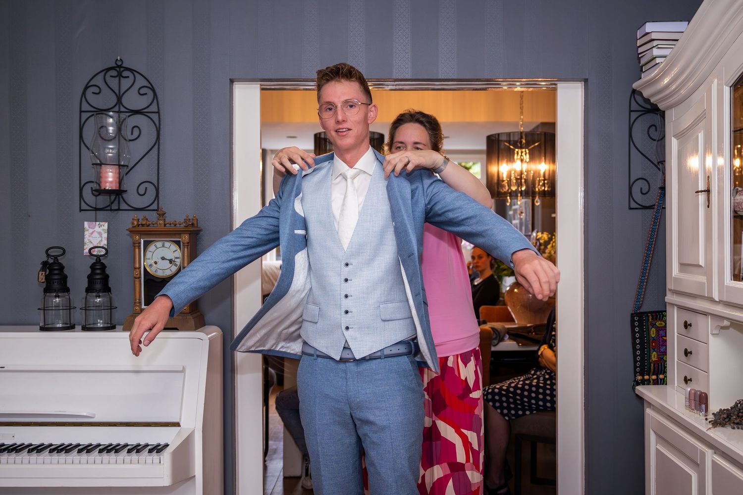 Person in formal attire being fitted for clothing in elegant room with piano.