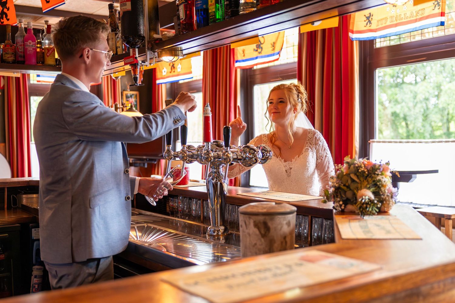 A couple in wedding attire stands at opposite sides of a rustic bar counter.