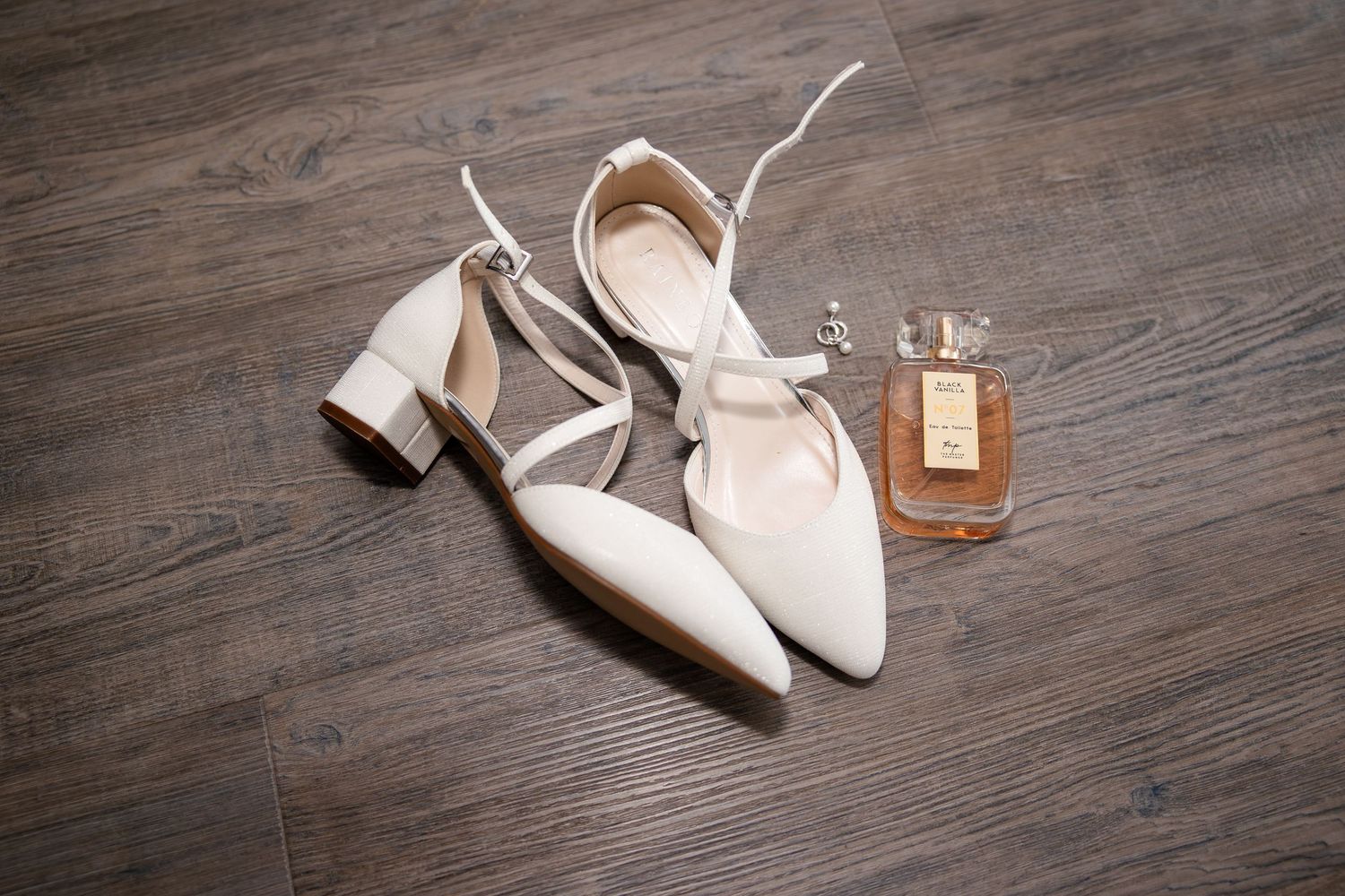 Wedding shoes and accessories arranged on wooden flooring.