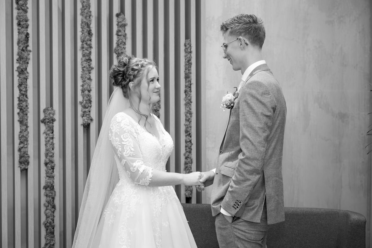 A black and white wedding photo of a couple sharing an intimate moment against a decorative wall.