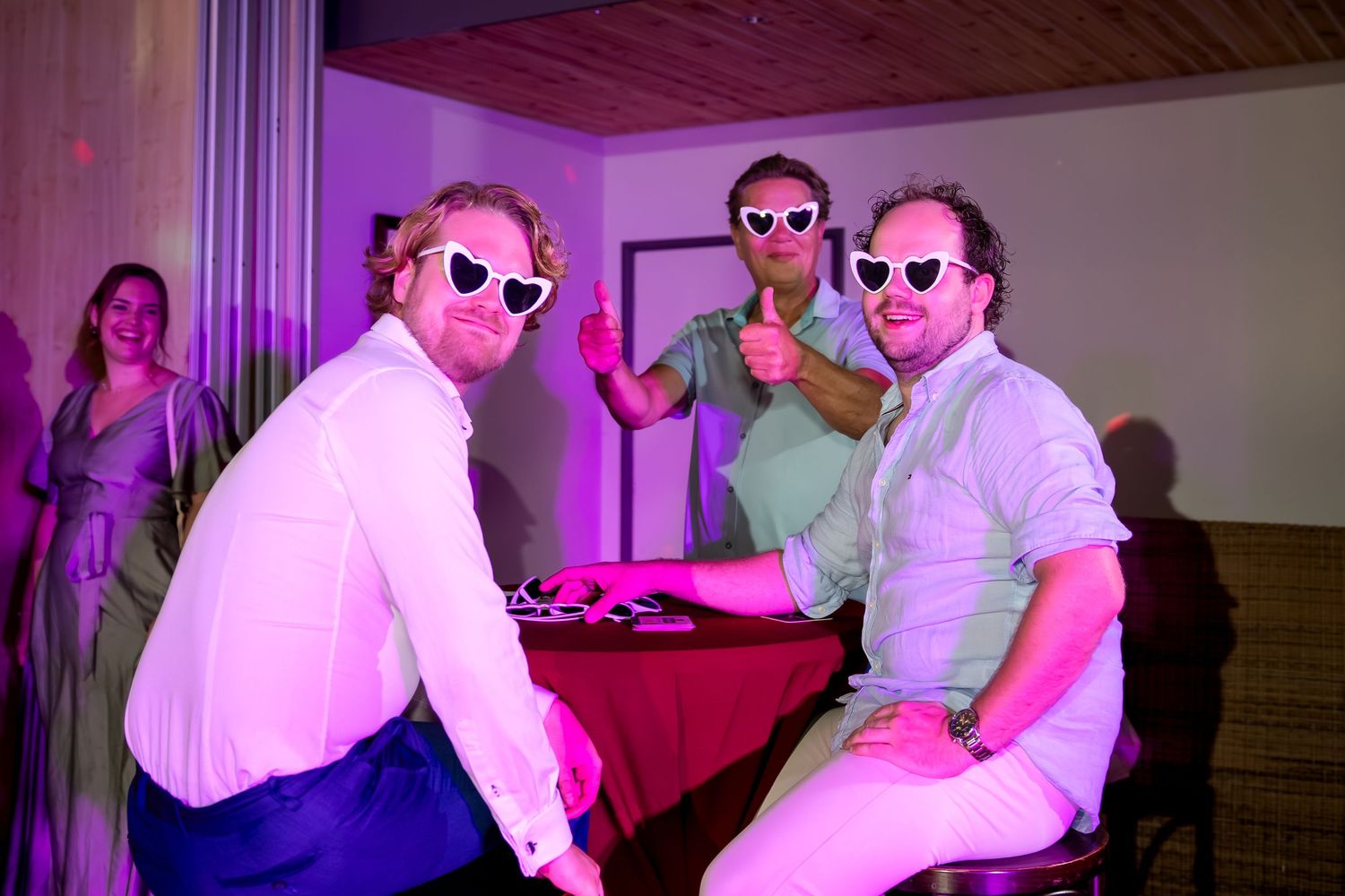 Wedding reception party with pink lighting and guests wearing sunglasses on the dance floor.