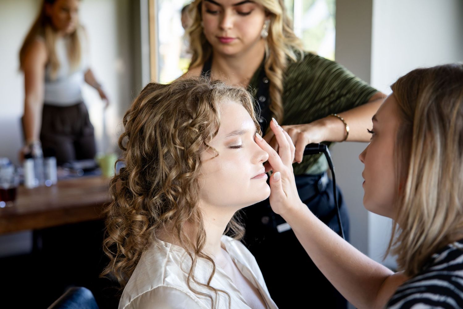 Hair and makeup preparation scene with soft natural lighting.