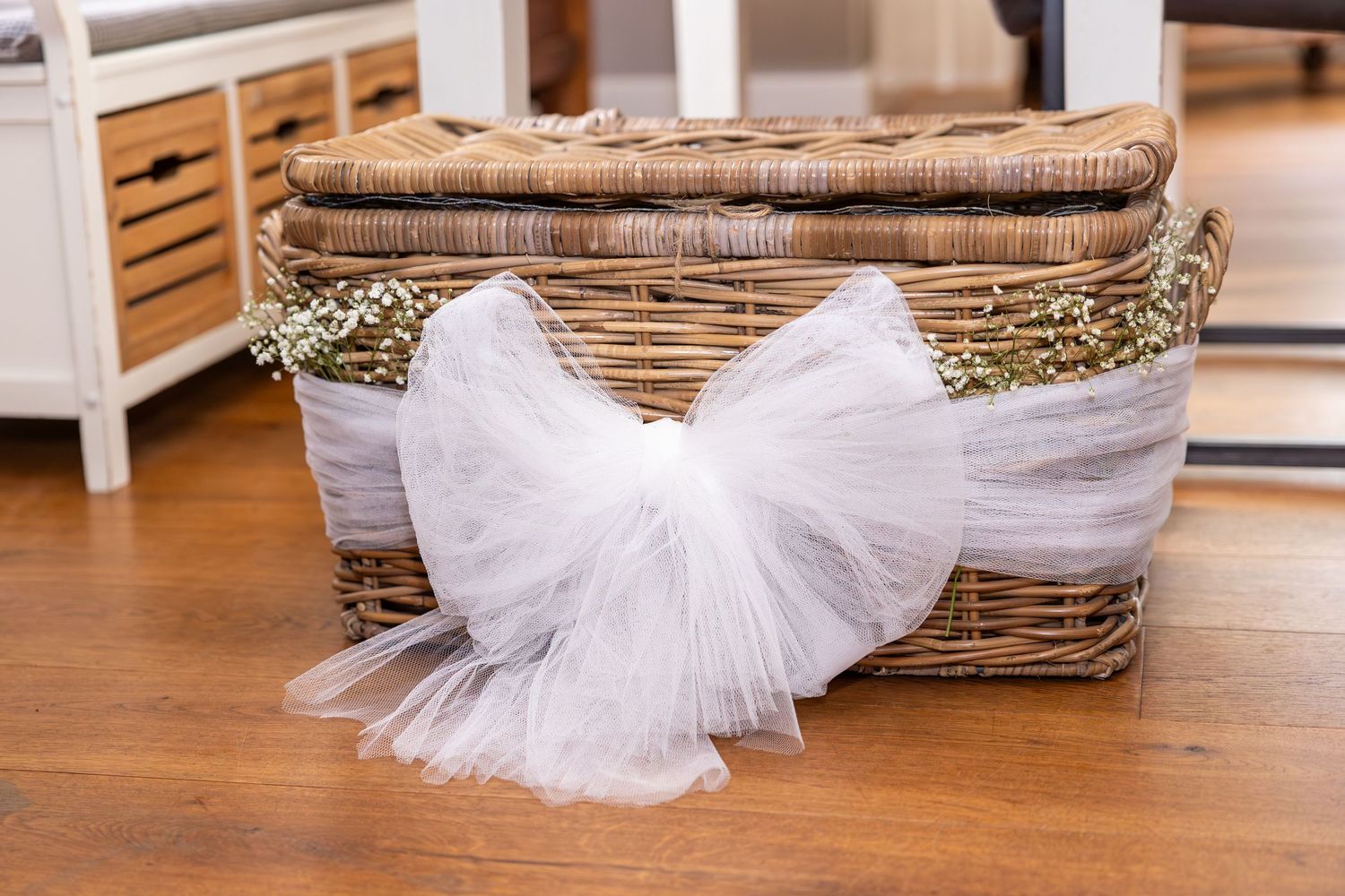 White tulle bow decorating wicker basket on wooden floor.