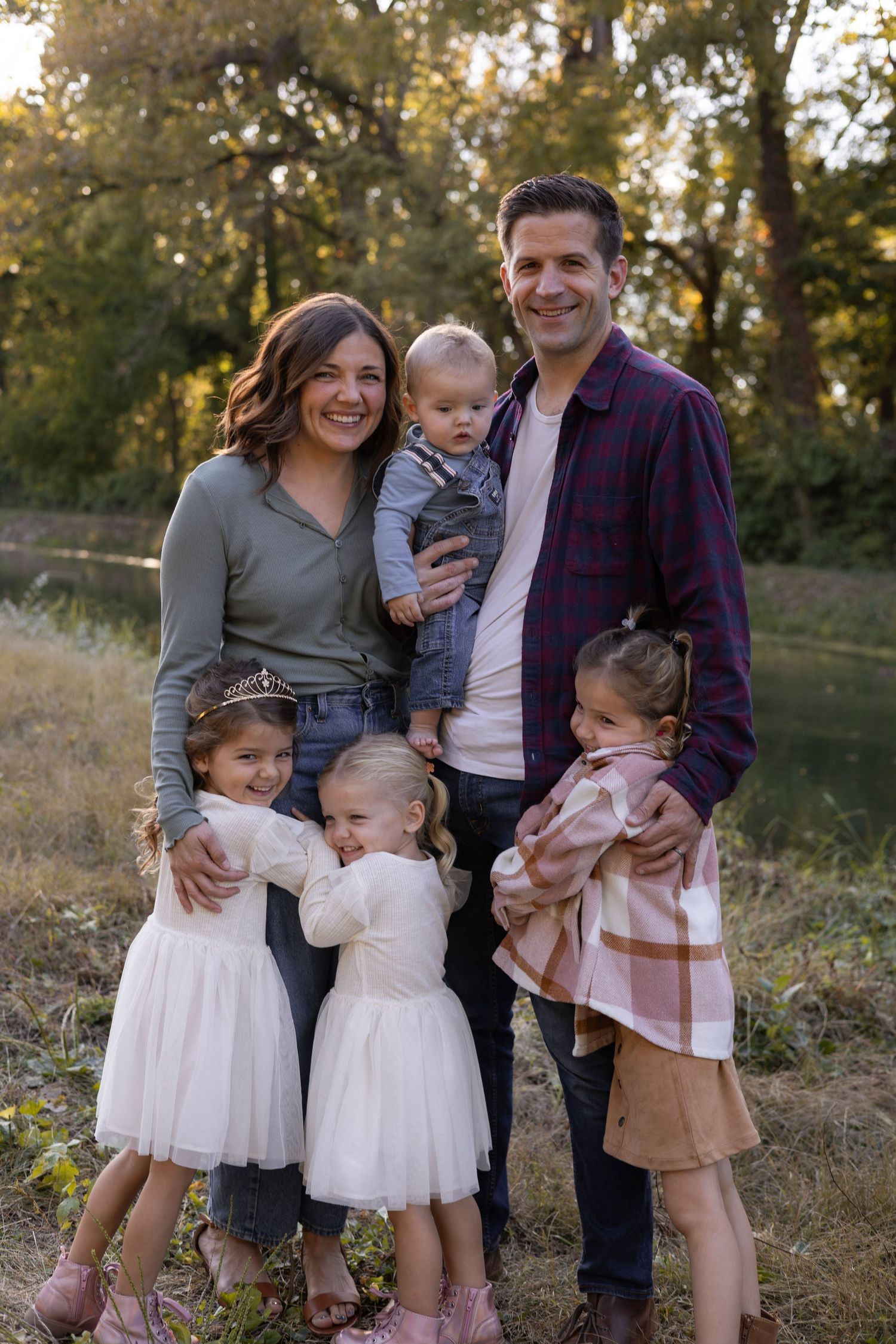 Smiling family of six poses together in a sunlit outdoor park setting.