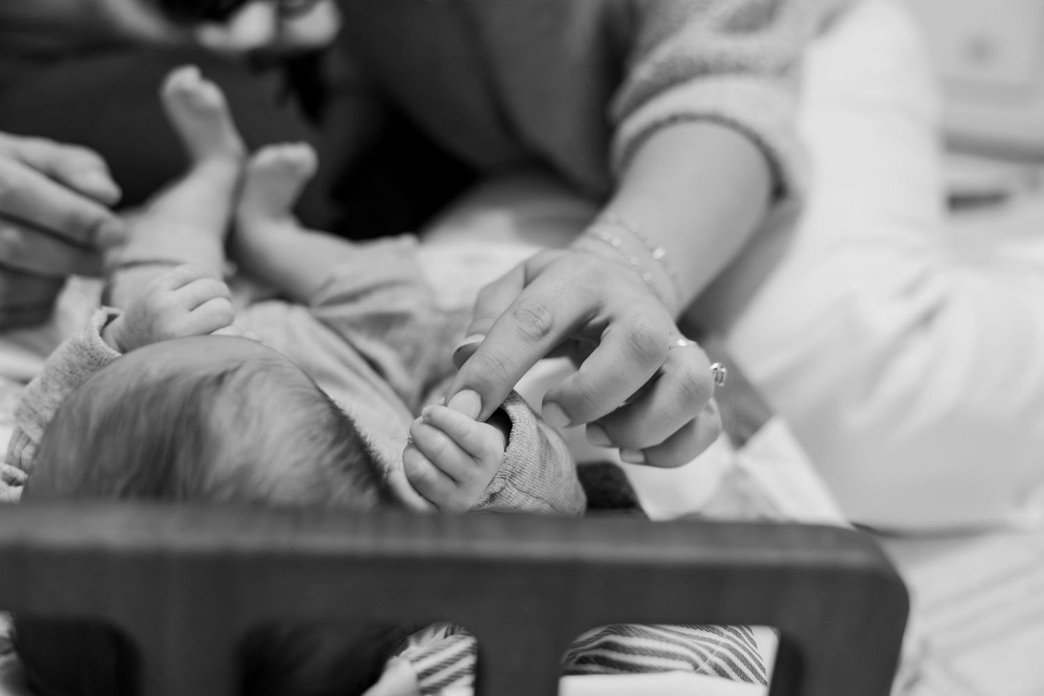 Black and white photo of newborn baby grasping mothers hand in wooden crib.
