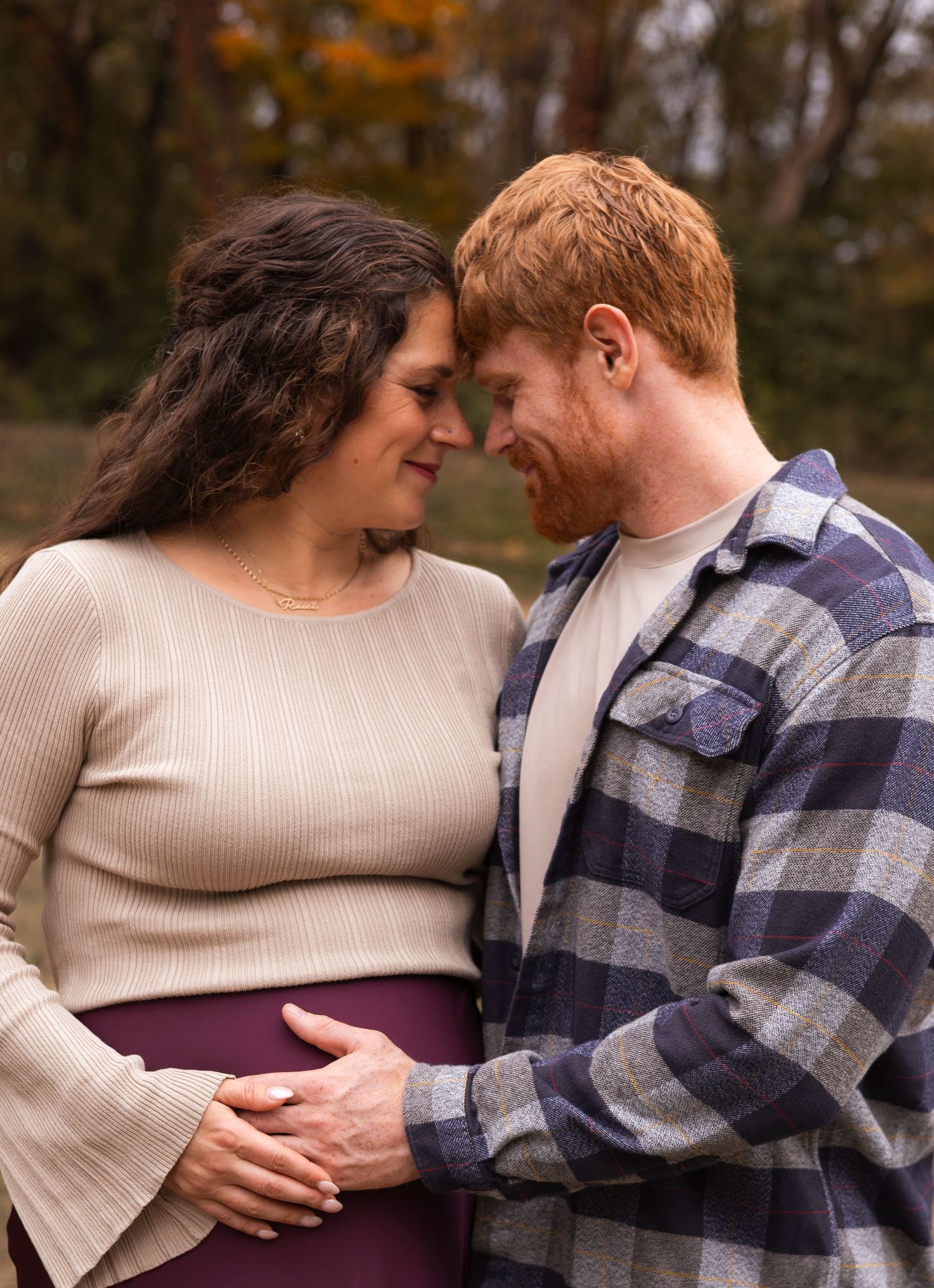 Expectant couple tenderly touch foreheads while cradling pregnant belly during autumn maternity photo session.