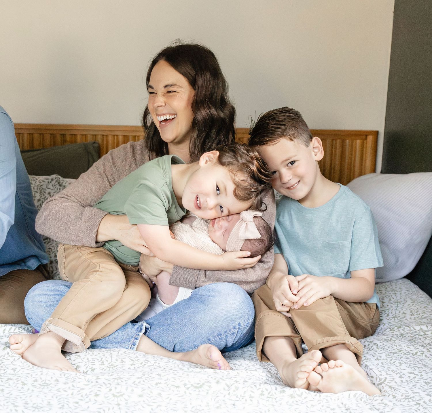 Smiling mother sits on bed with three children including newborn baby girl.