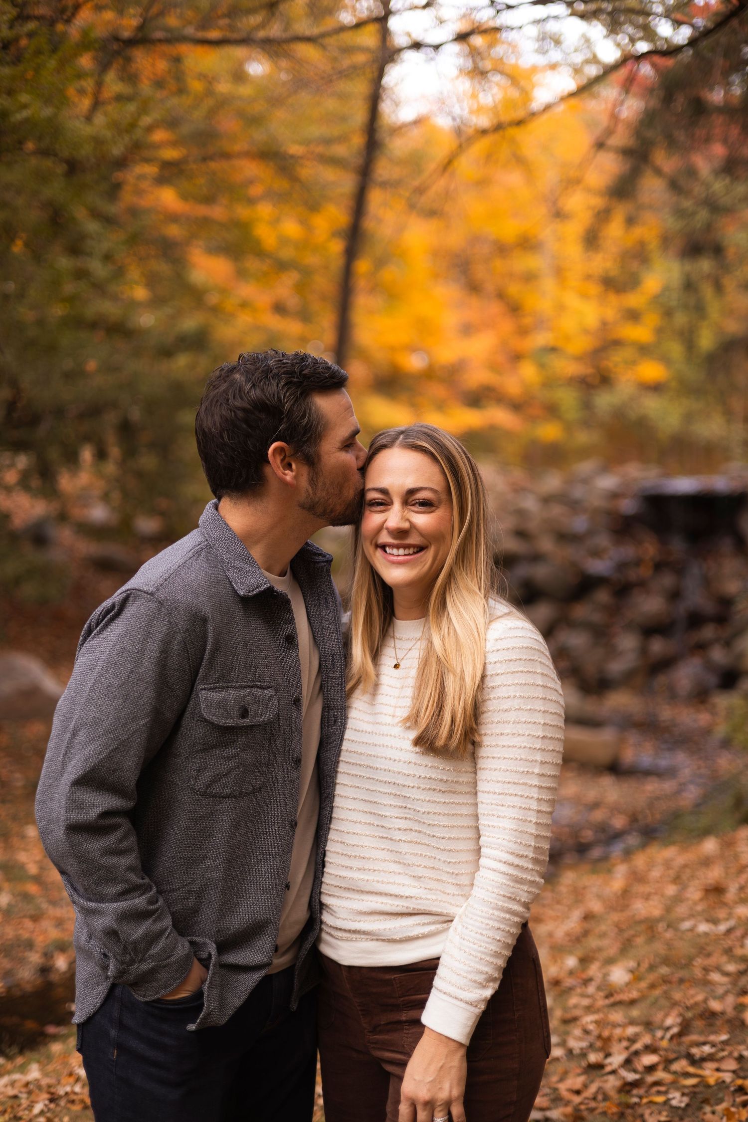 Man whispering to laughing blonde woman in an autumn forest.