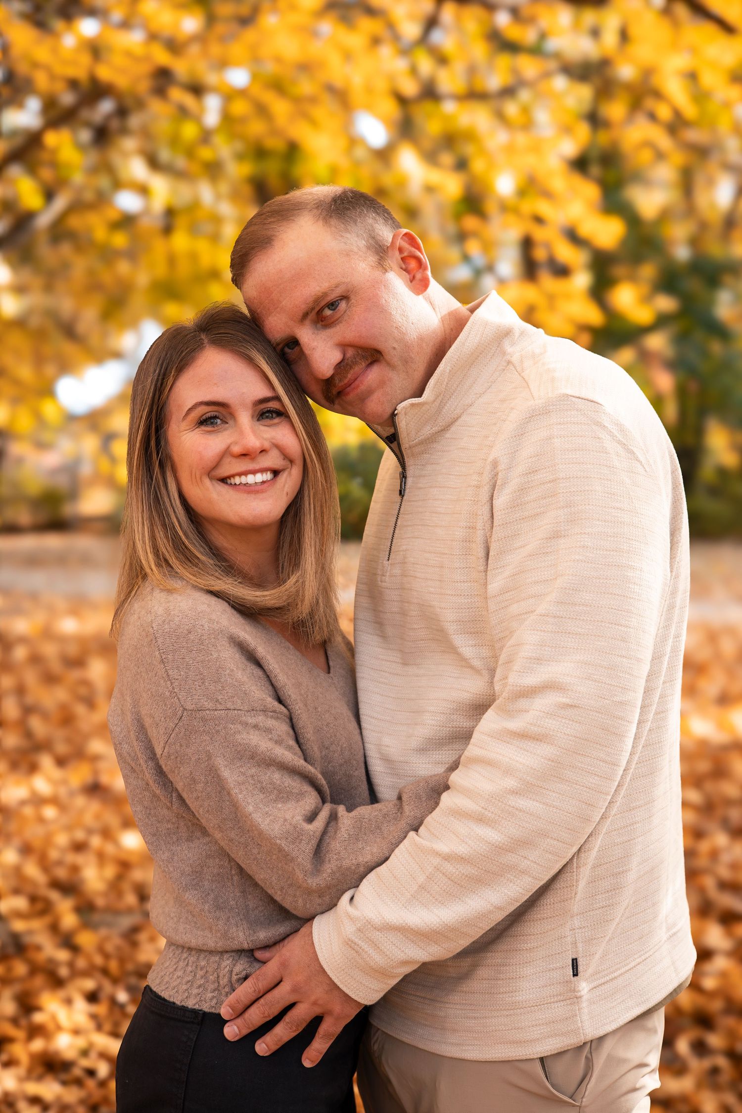 Smiling couple embracing in a park surrounded by fall foliage.