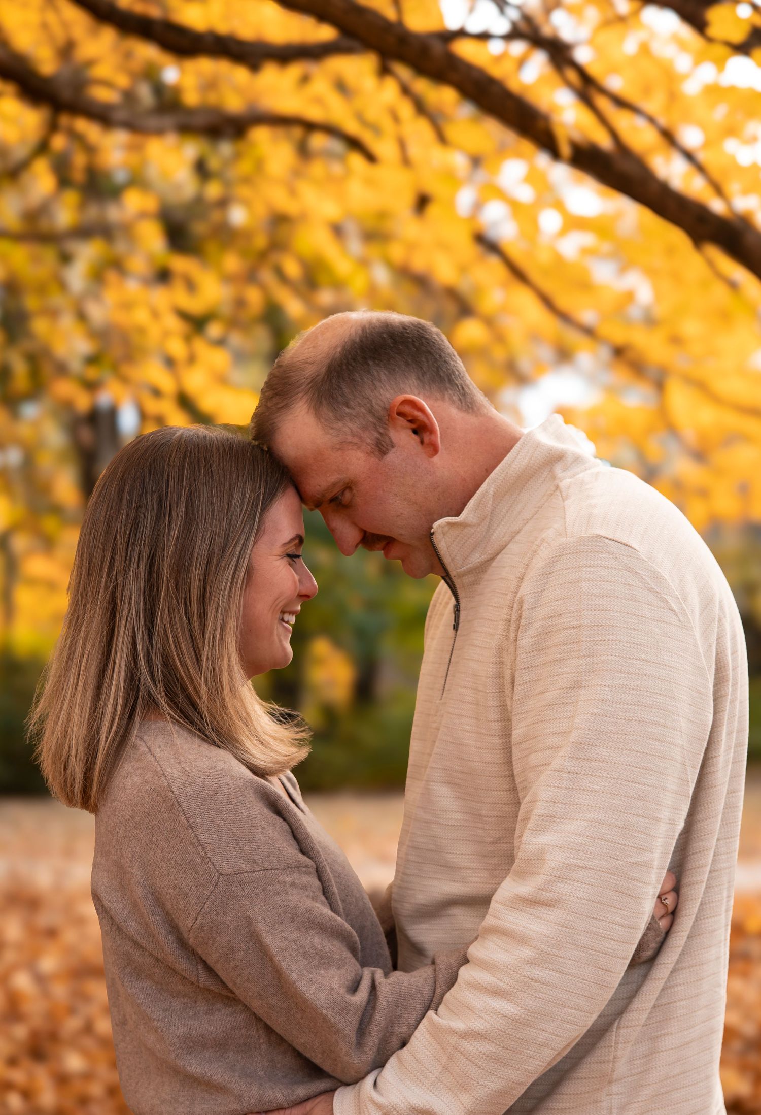 Couple sharing a tender forehead touch under golden autumn trees.
