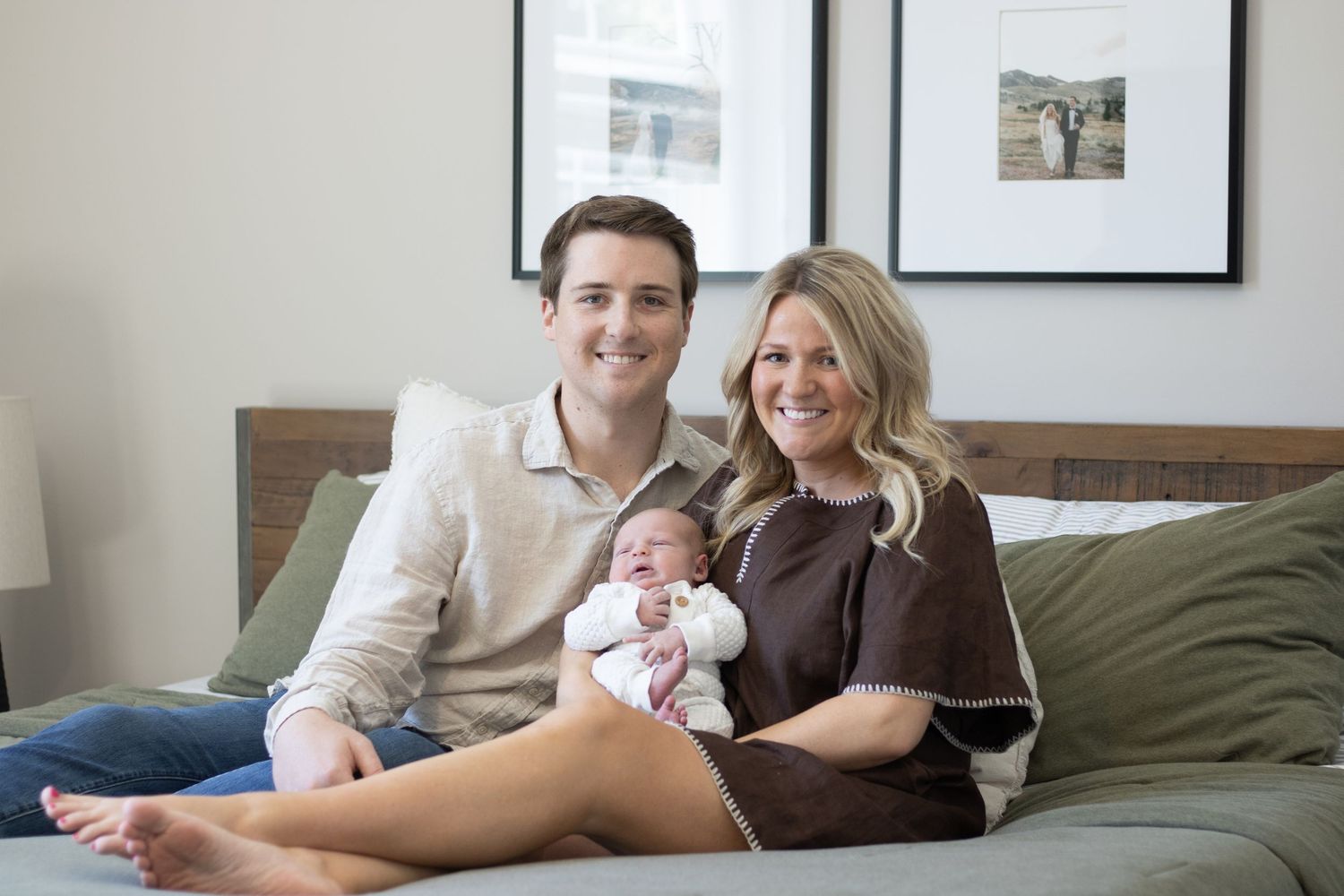 Smiling couple sits on a couch together holding their newborn baby.