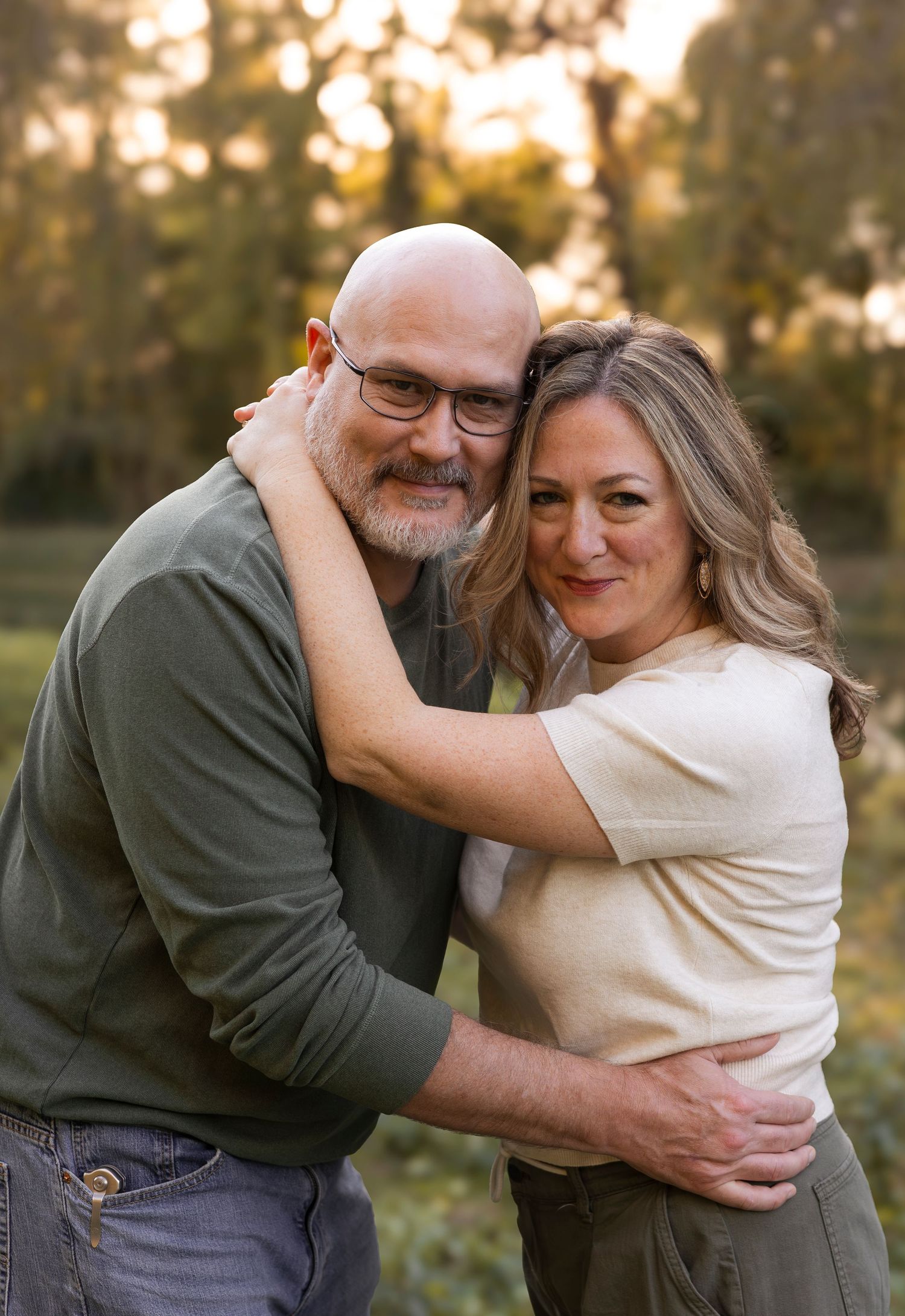 A smiling middle-aged couple embracing warmly outdoors in a sunlit park during golden hour.