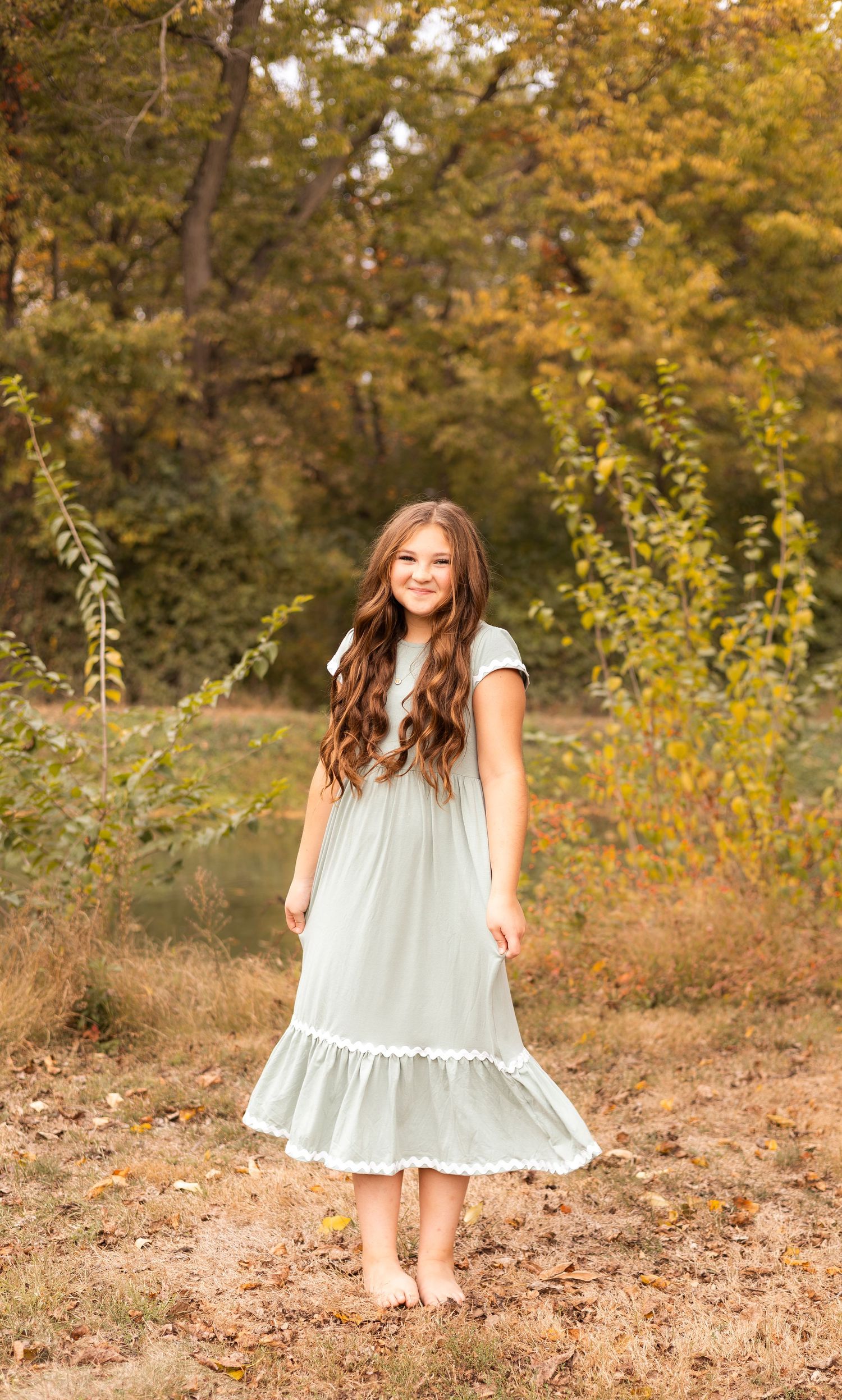 Young girl in mint ruffle dress standing barefoot in autumn outdoor setting.