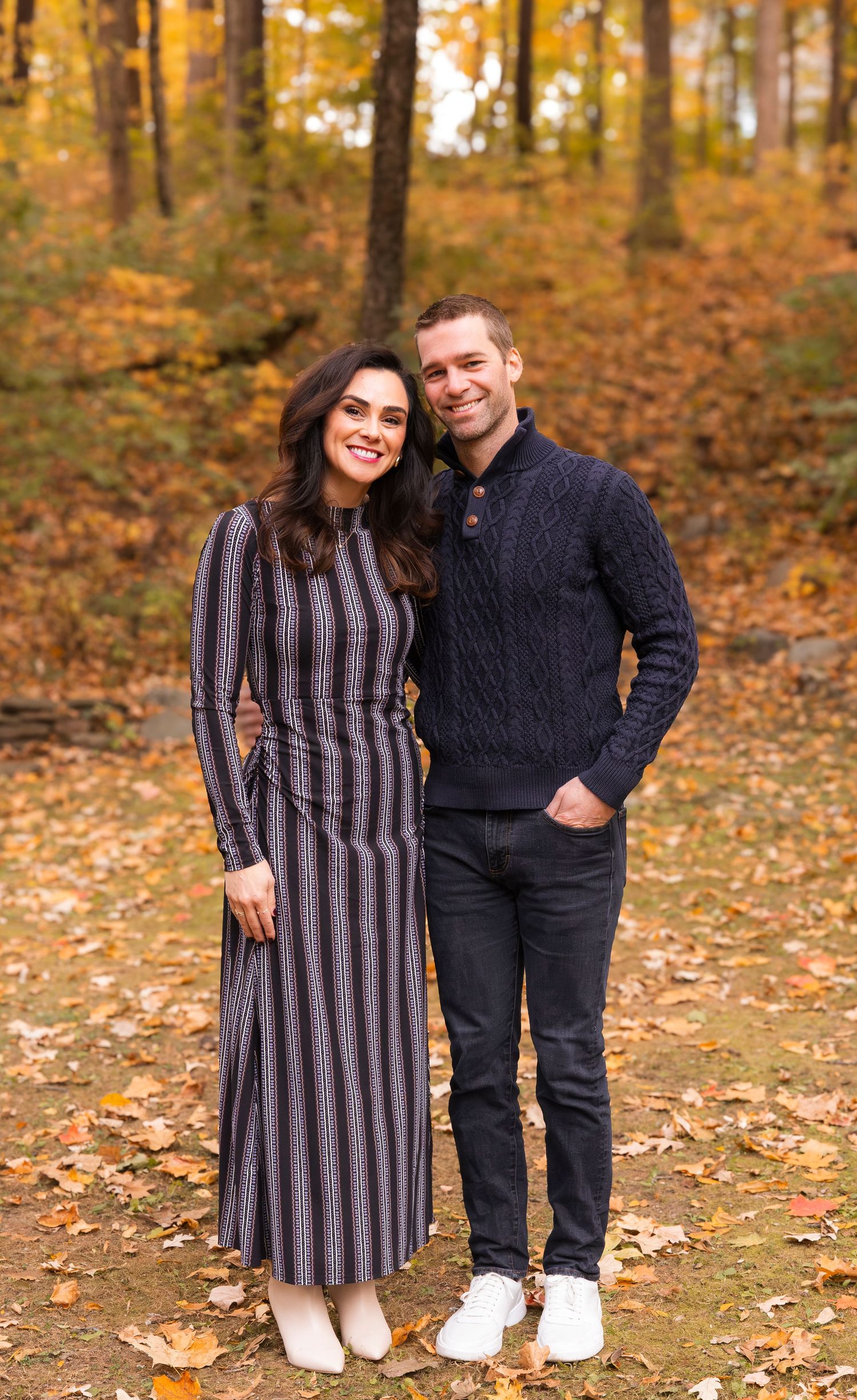 Stylish couple posing together in a forest with fall foliage.