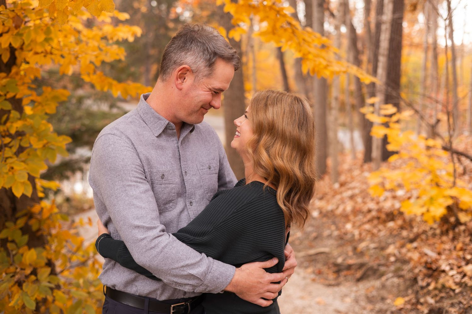 Couple embracing and smiling at each other among golden fall foliage.