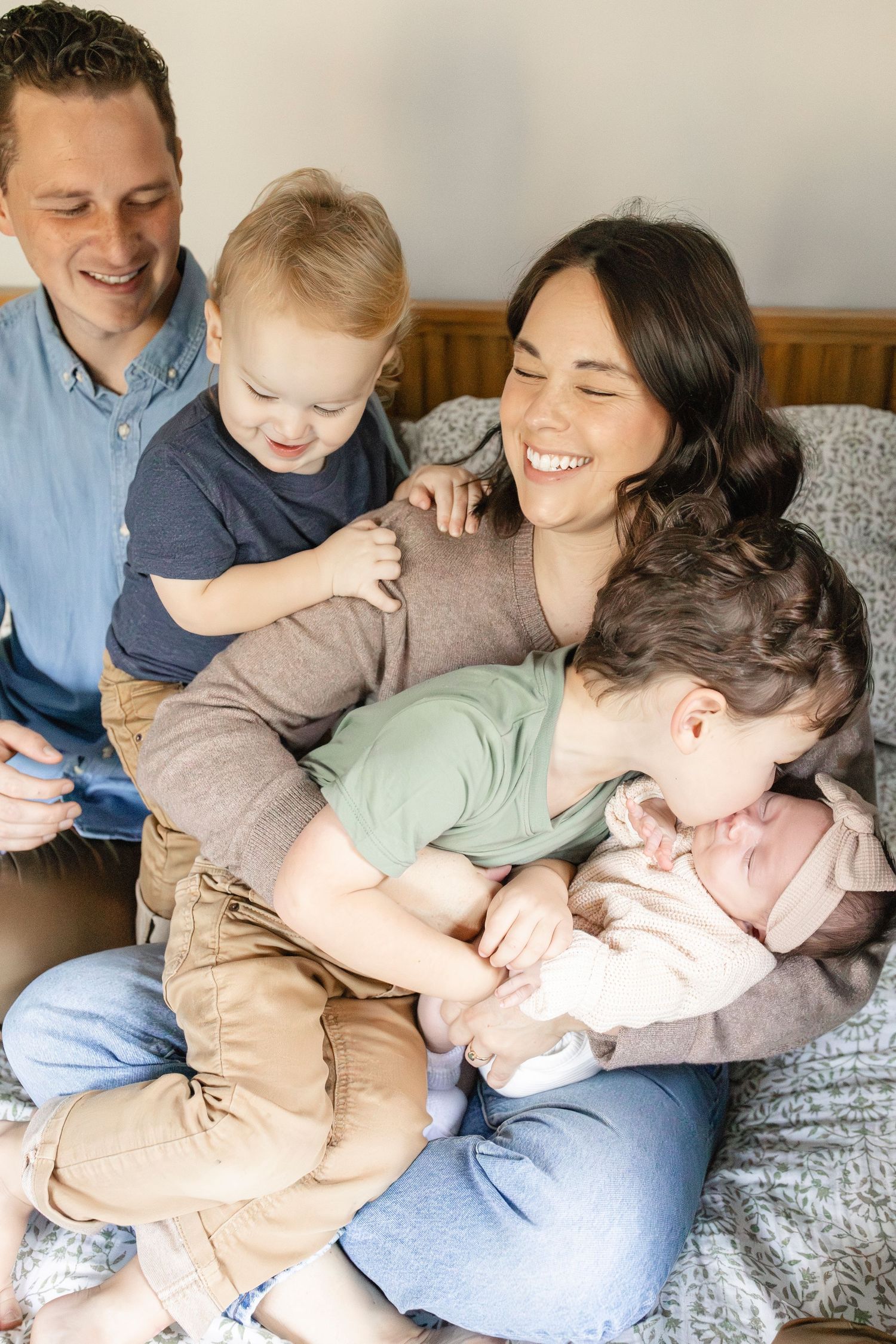 Happy family of five laughing together on a bed with their newborn baby girl.
