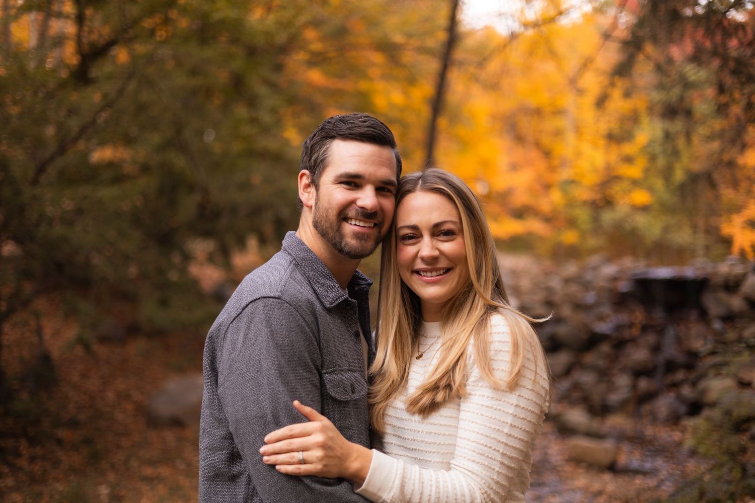 Smiling couple embracing in a colorful autumn forest setting.