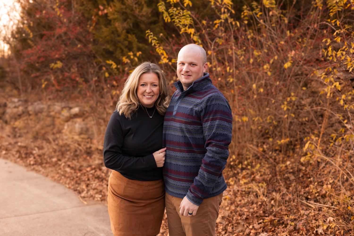 Couple smiling together on autumn path surrounded by colorful fall foliage.