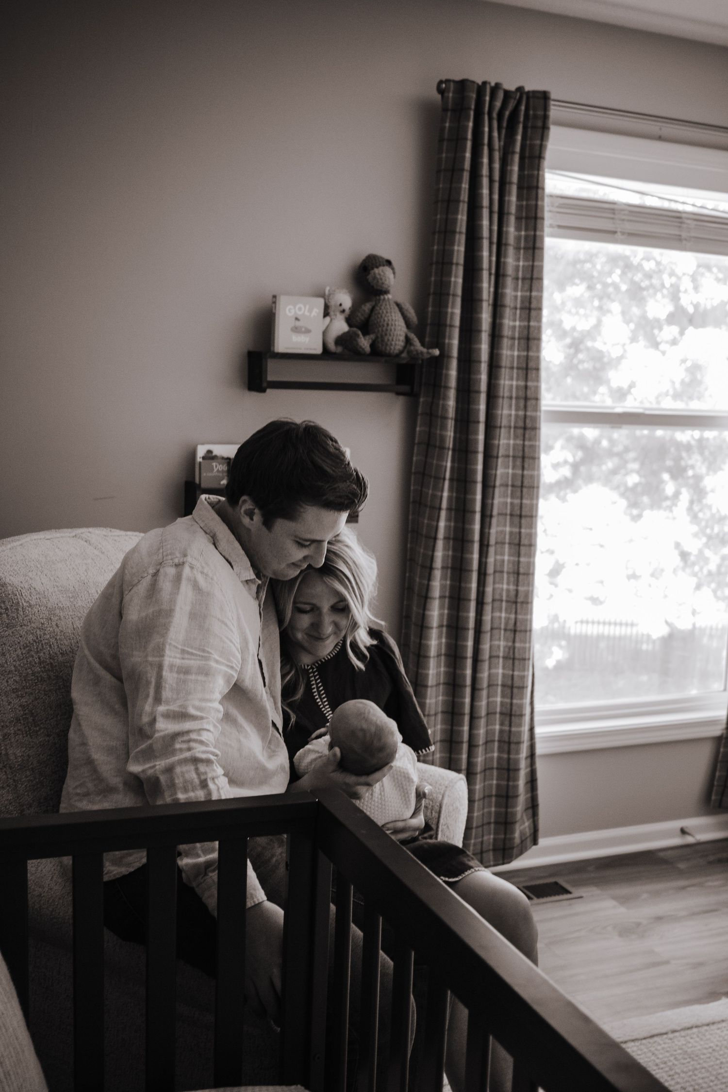 Black and white photo of couple sitting together in nursery lovingly holding newborn baby.