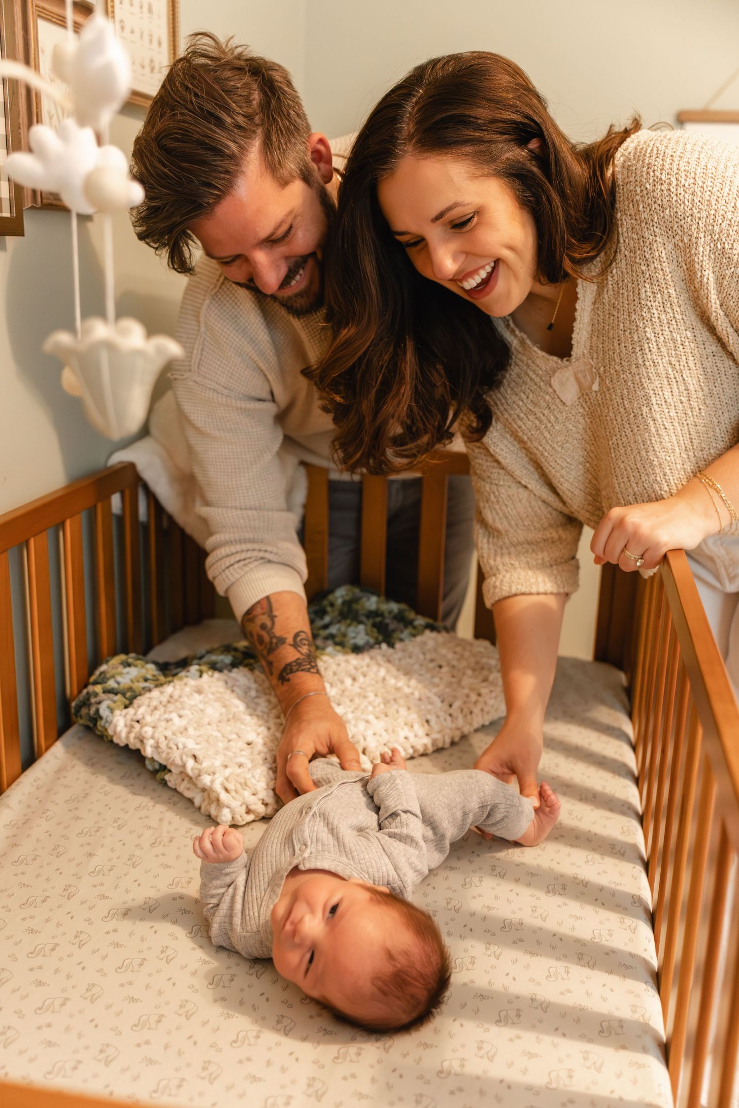 Happy parents smiling and playing with their newborn baby lying in a wooden crib.