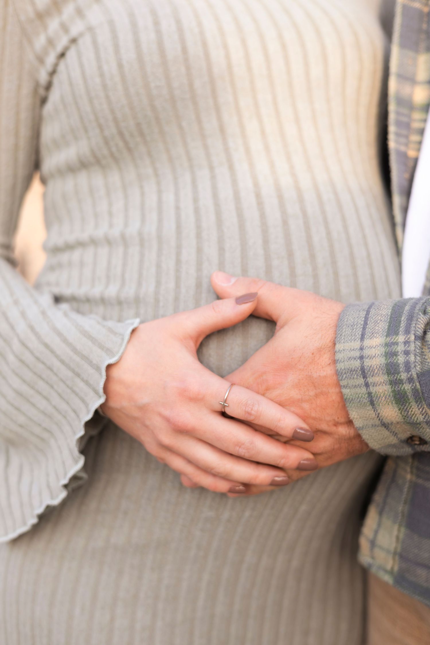 Close-up of couple holding hands on pregnant belly, woman wearing engagement ring in fall setting.
