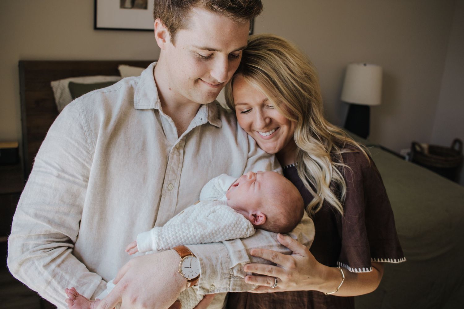 Smiling couple sharing a joyful moment while holding their newborn baby indoors.