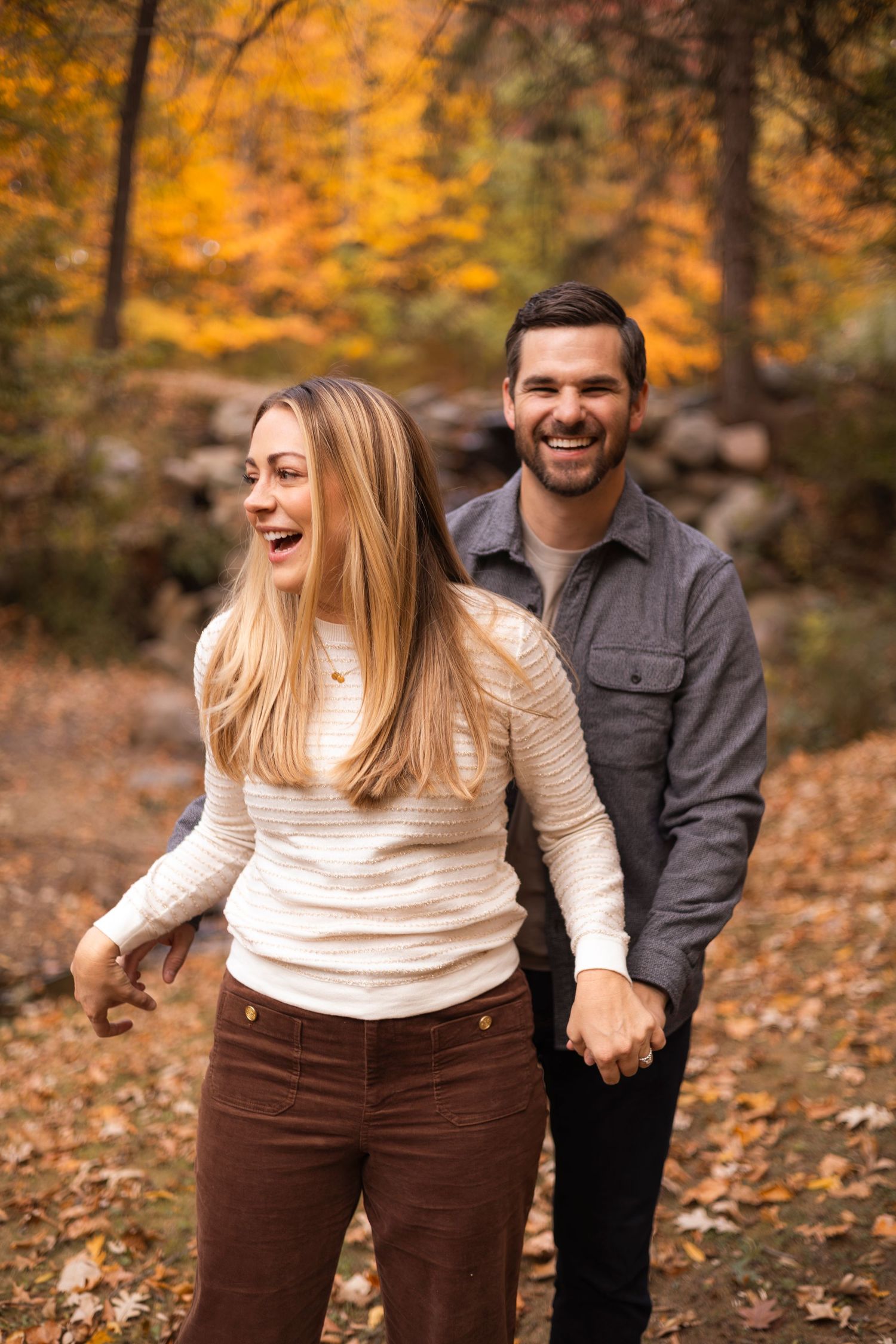 Laughing couple holding hands while walking through fall foliage.