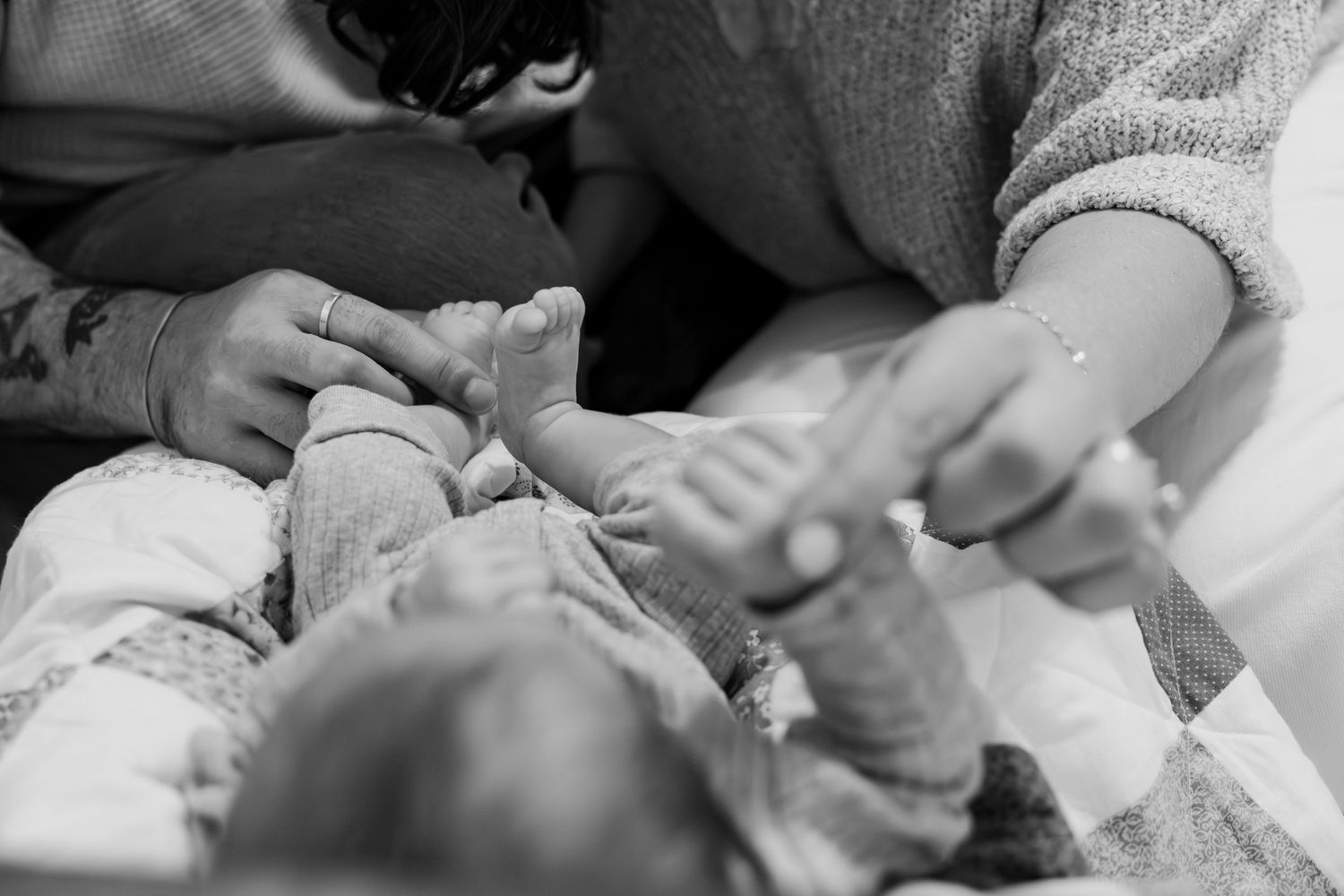 Black and white image of parents holding newborn babys tiny feet and hands gently.