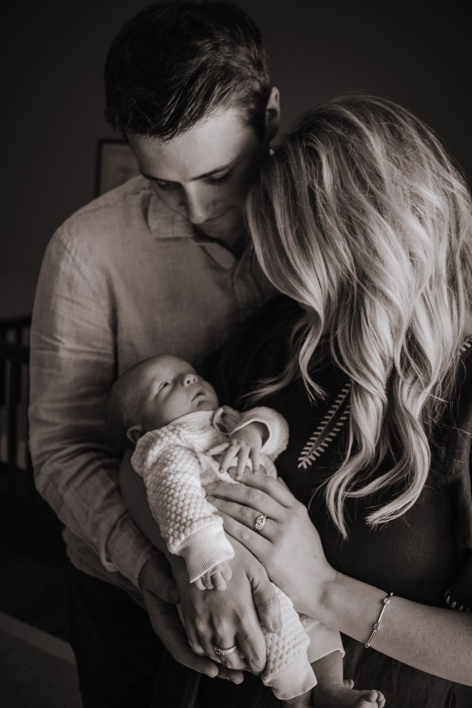 Black and white photo of couple sharing tender moment while holding their newborn baby.