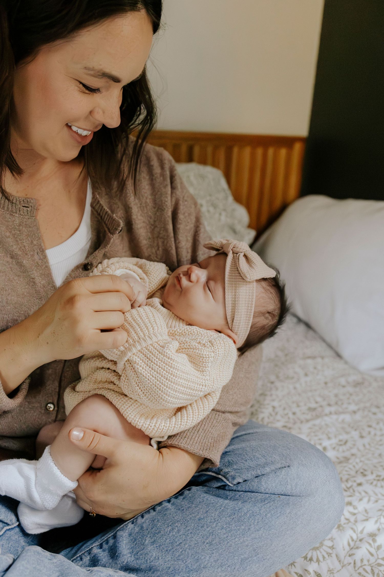 Mother smiles lovingly at her newborn baby girl in knit outfit and bow headband.