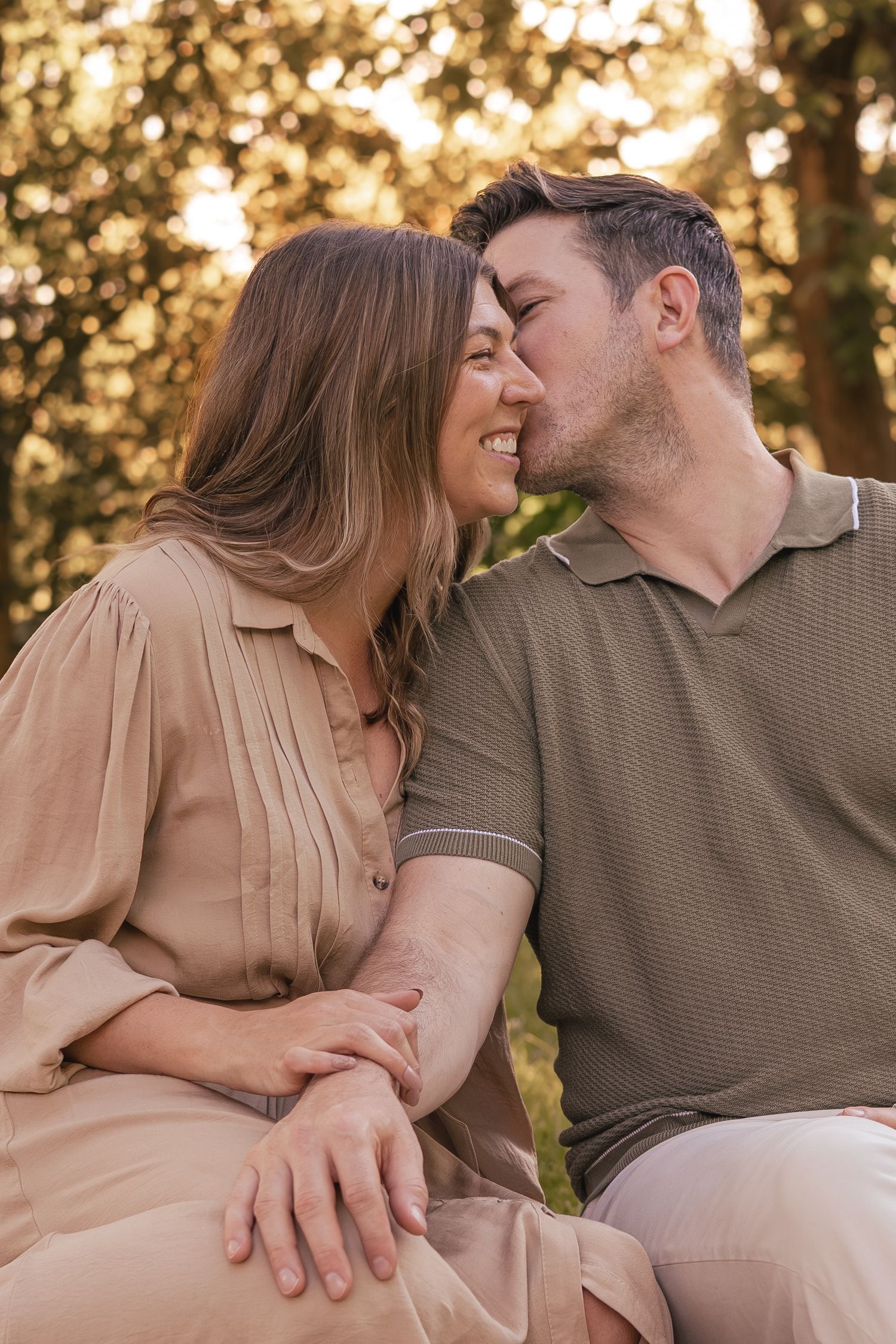 Affectionate couple sitting closely together sharing a tender kiss in golden sunlight.