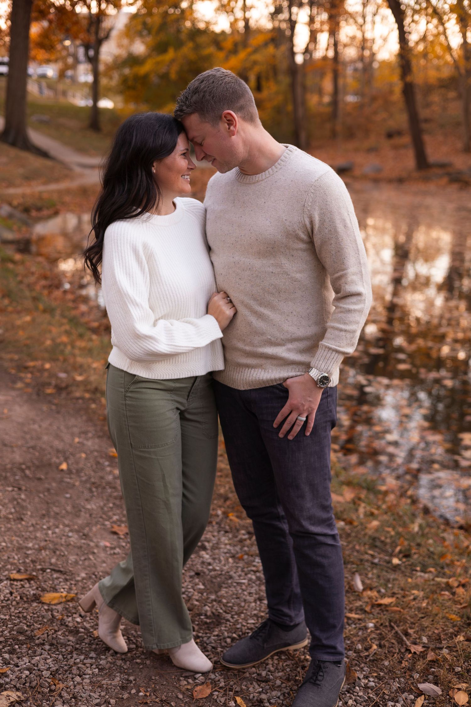 Romantic couple leaning close together beside a tranquil autumn pond.